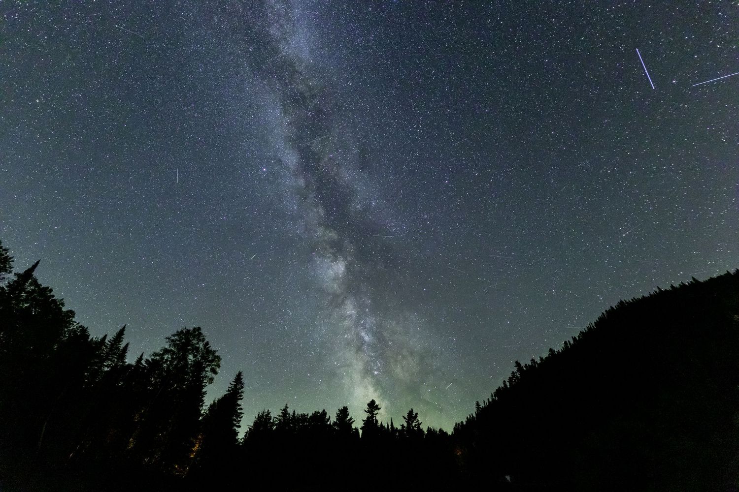 Milky Way galaxy visible in night sky above silhouetted forest treeline.