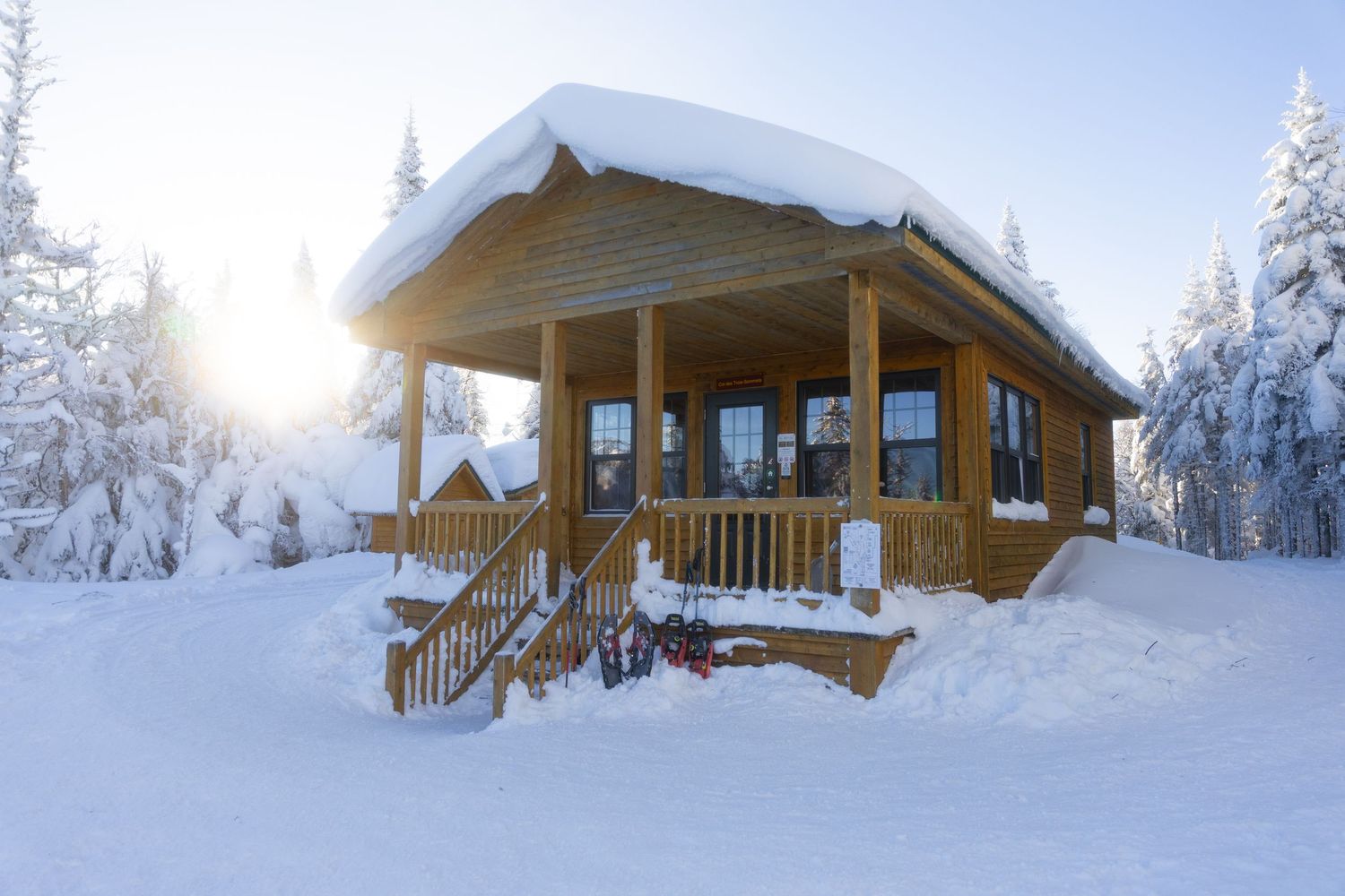Snow-covered wooden cabin with a porch surrounded by winter forest scenery.