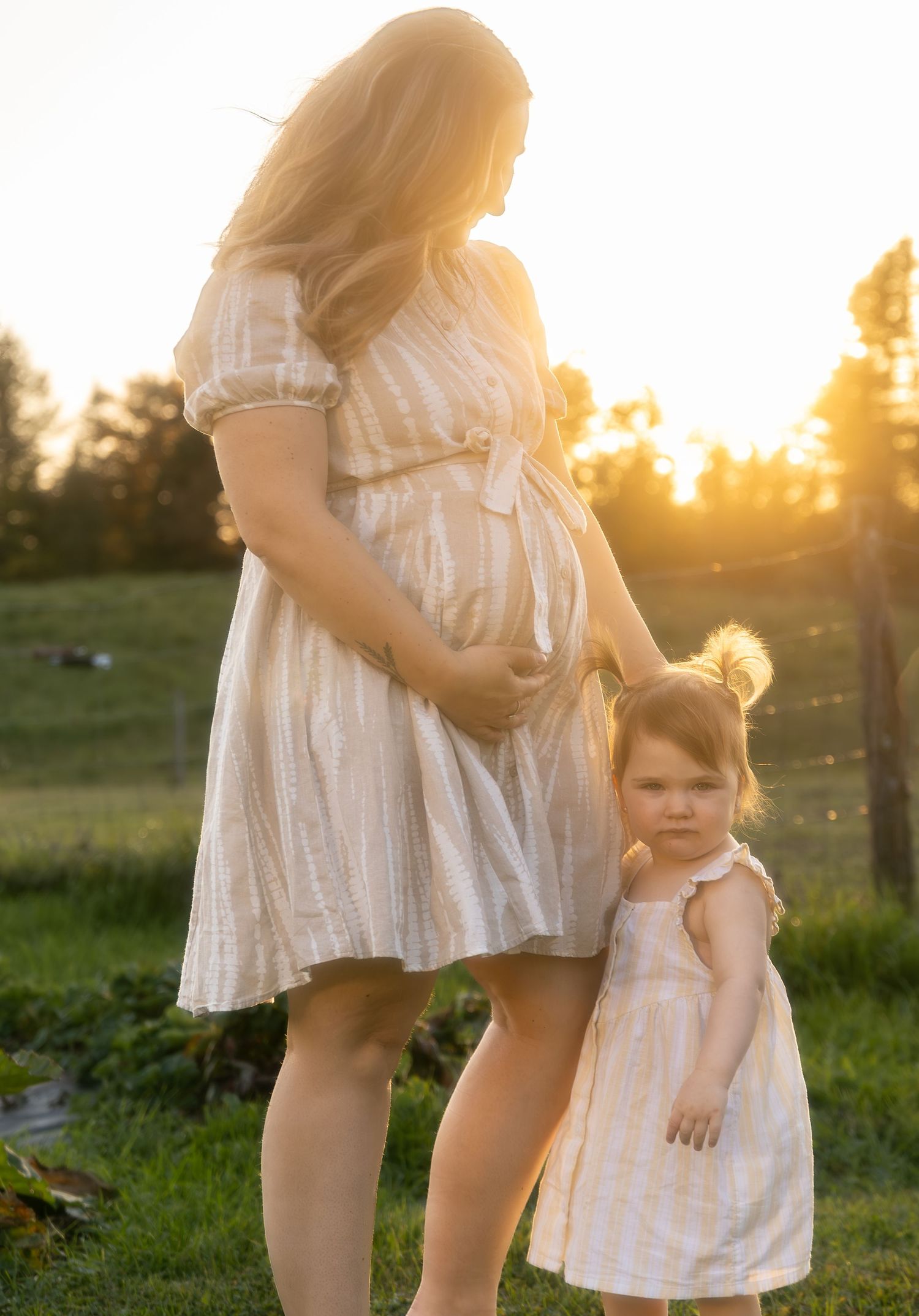 Mother and child in white dresses standing in sunlit field.