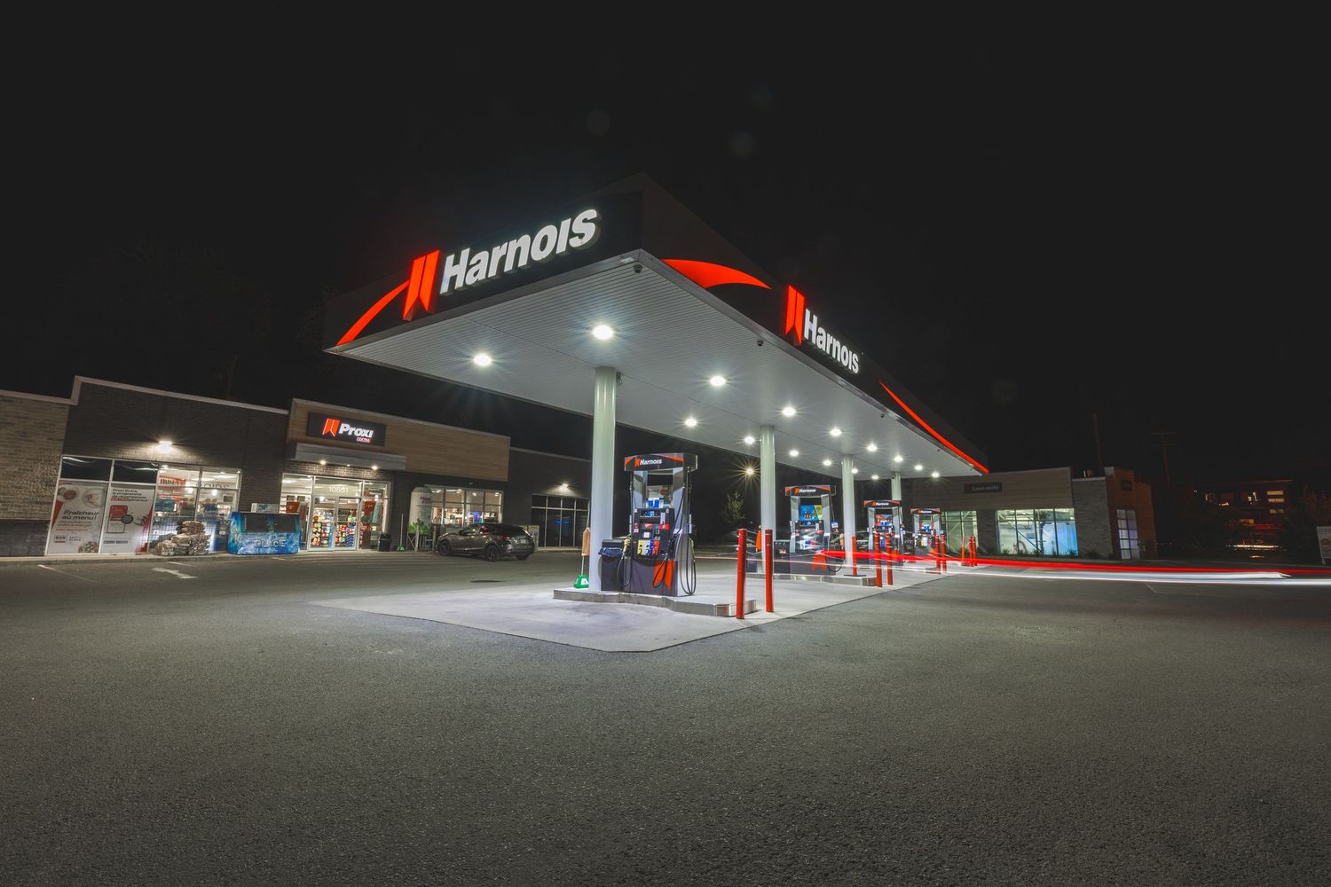 A panoramic nighttime view of a well-lit gas station with red and white exterior illumination.