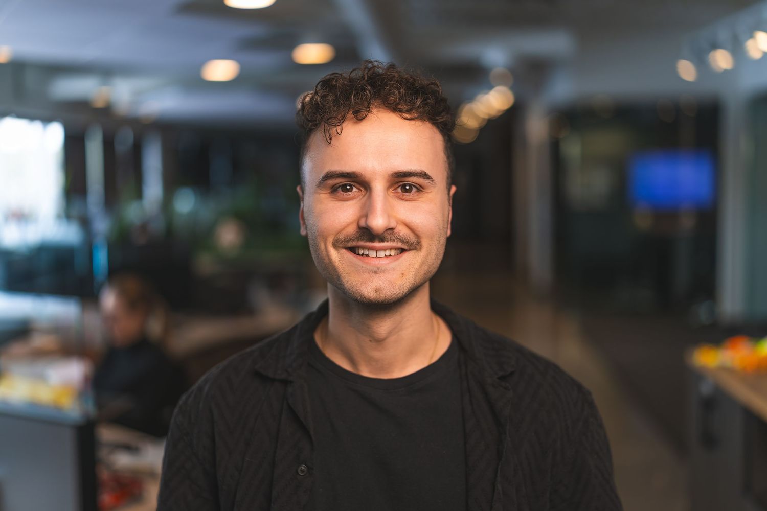 Portrait of person in dark clothing against blurred office background.