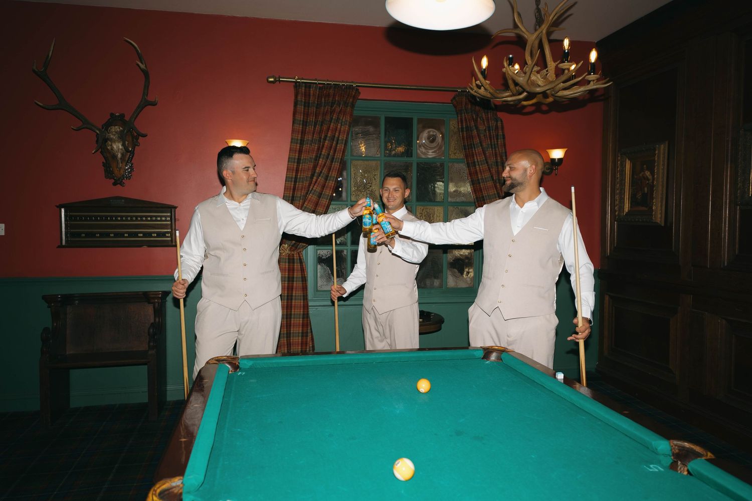 Three men in matching suits celebrate around a green billiards pool table in a rustic game room.