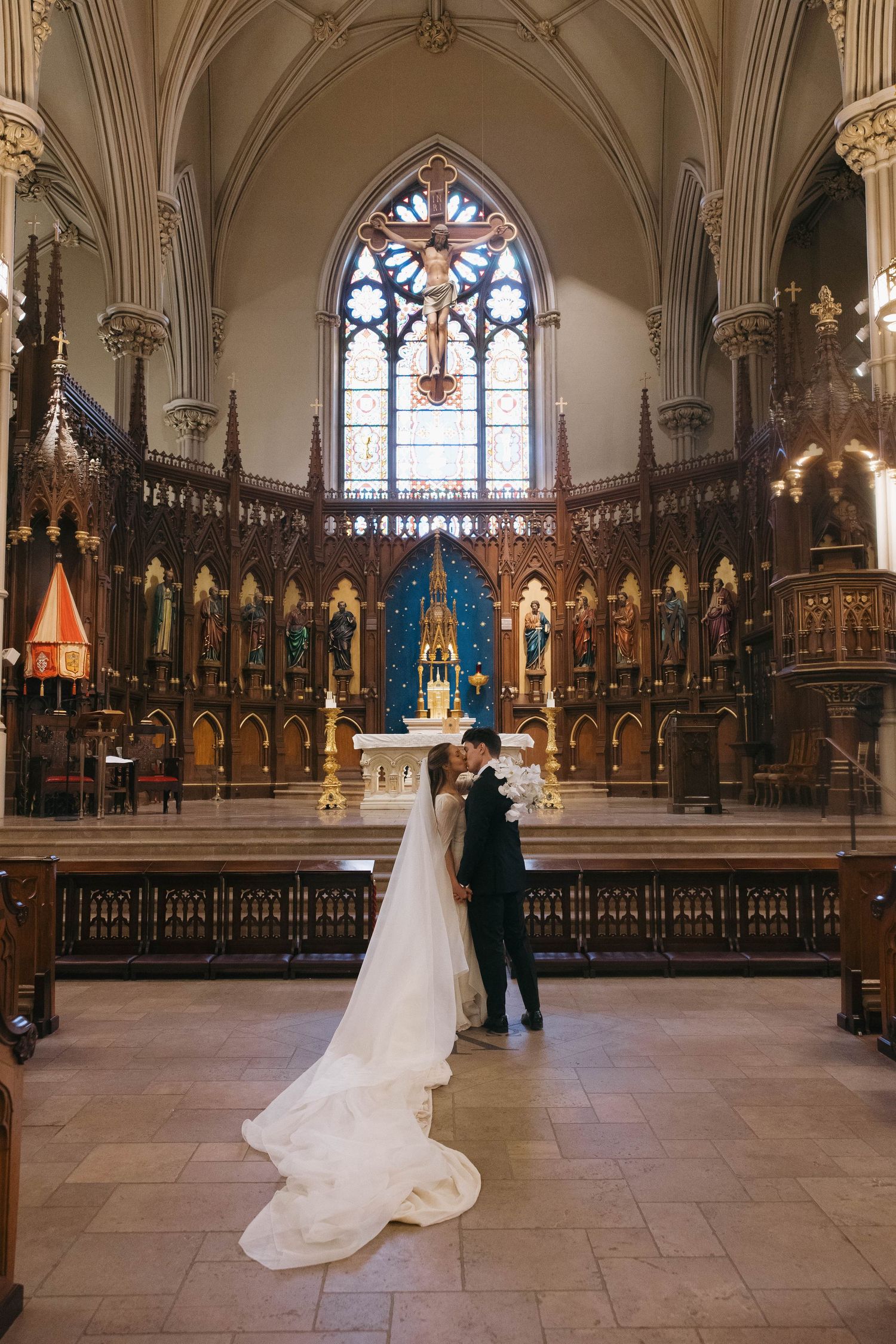 Bride and groom share a romantic moment at the altar of an ornate Gothic cathedral with stained glass windows.