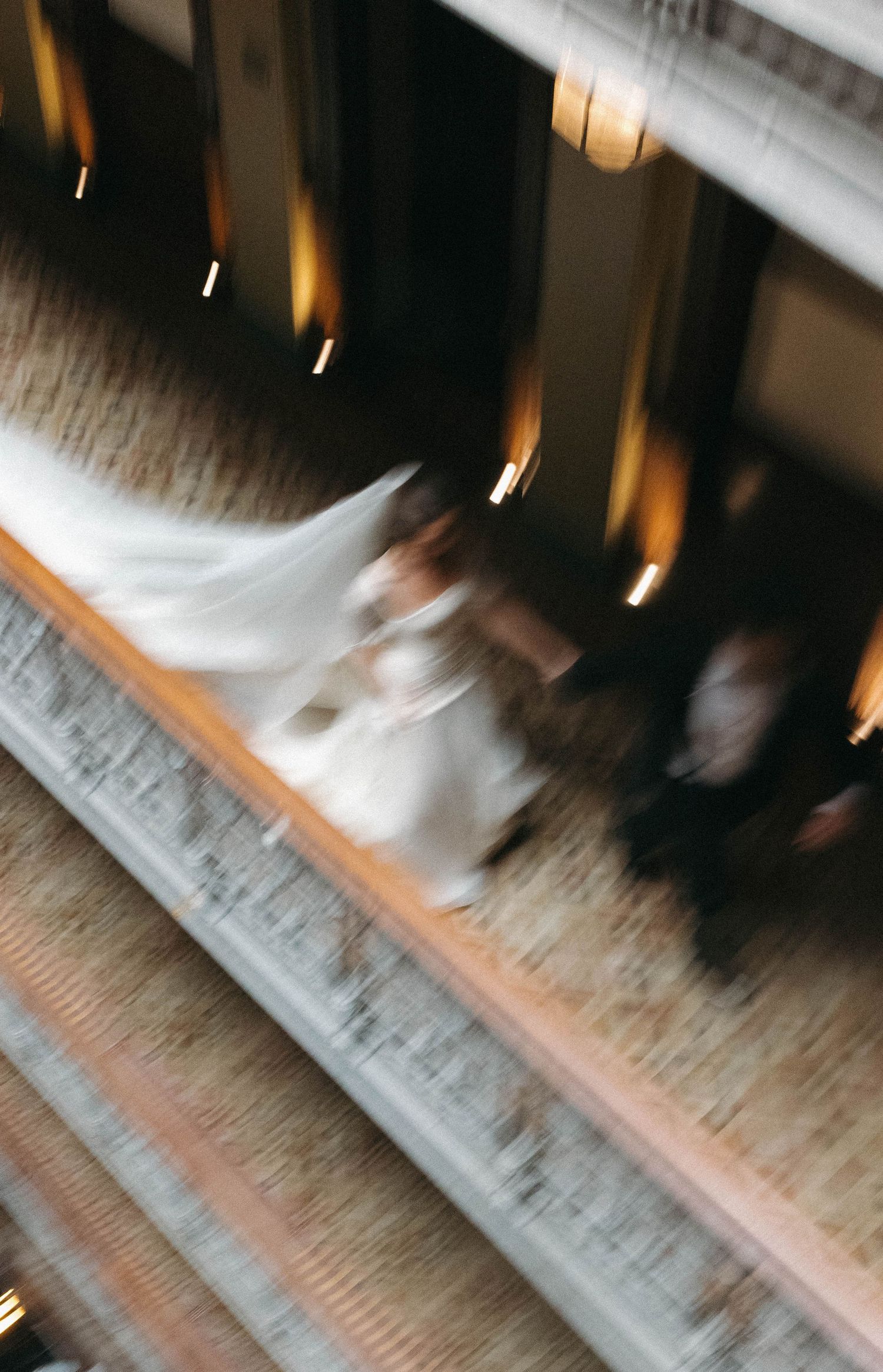 Blurred motion shot of a bride in a white gown and veil walking down stairs at an elegant wedding venue.
