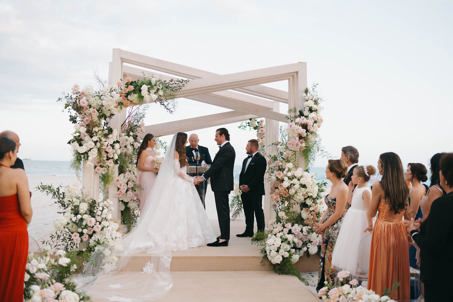 Wedding ceremony arch decorated with white flowers against a bright sky on the beach.