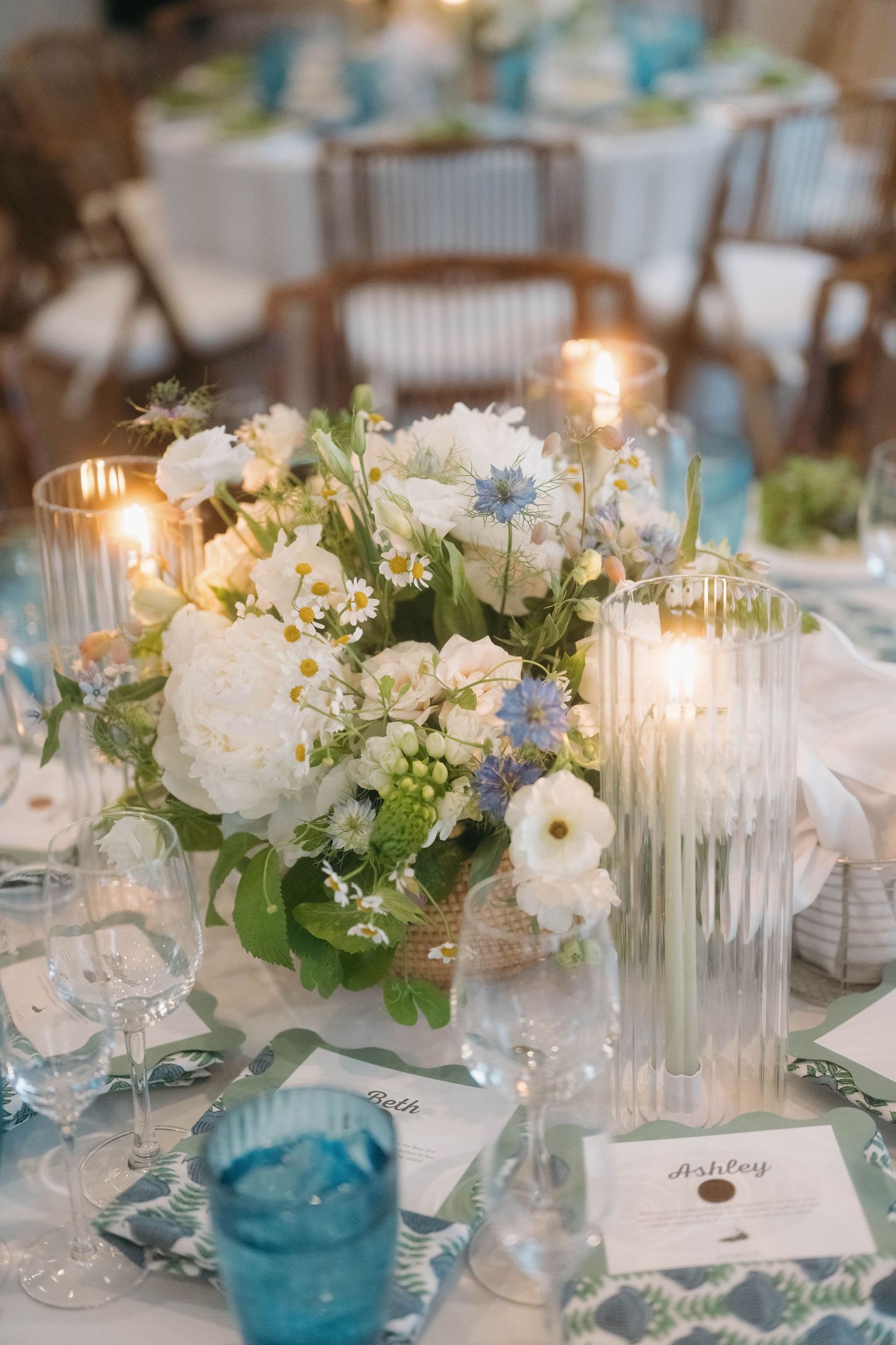 Elegant table setting with white flowers, blue glassware, and lit candles for a wedding reception.