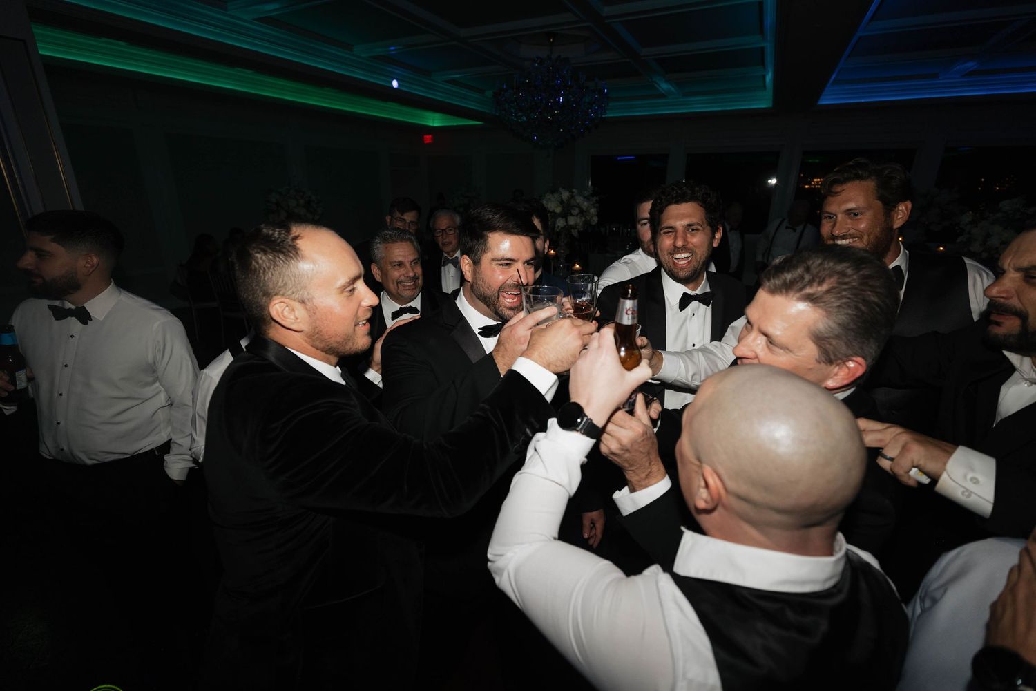 Wedding reception guests in formal wear dancing and celebrating on a dark dance floor.
