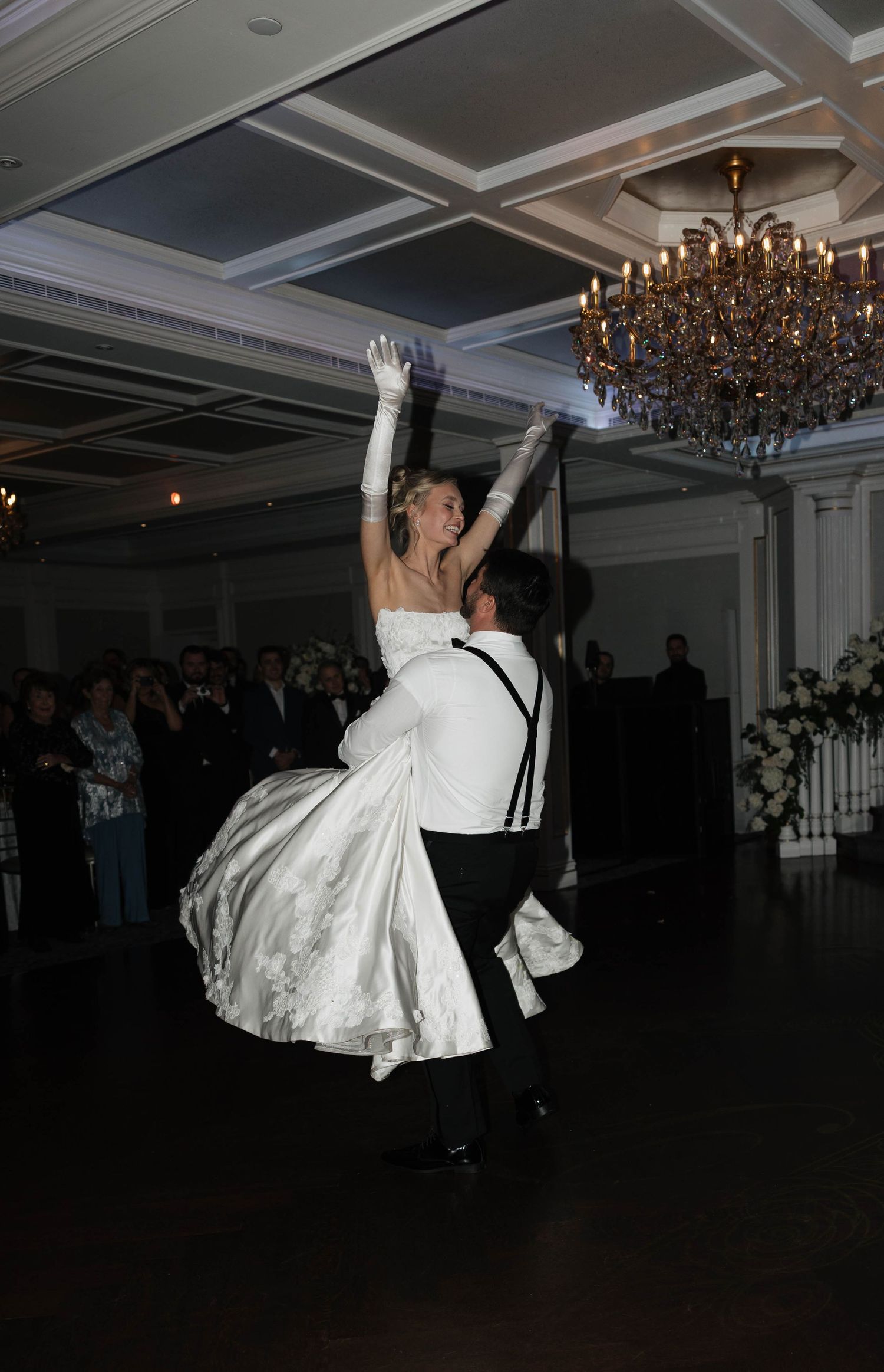 A dramatic dance lift silhouetted against chandeliers during a wedding reception.