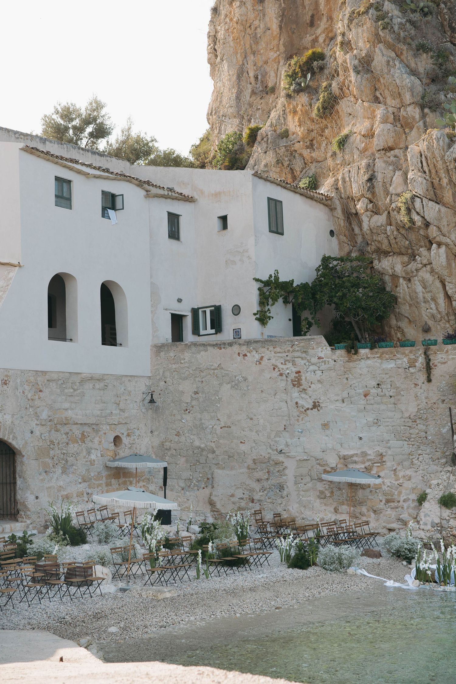 White stone buildings nestled against dramatic rocky cliffs in a Mediterranean coastal setting.