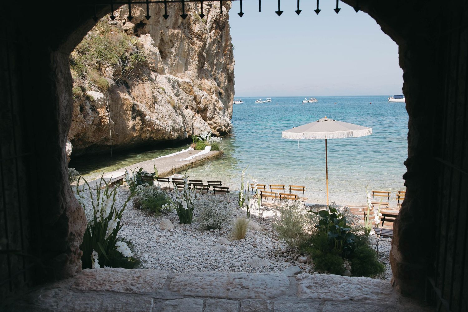 Rustic stone walls and arches frame a scenic Mediterranean beach view with crystal clear turquoise waters.