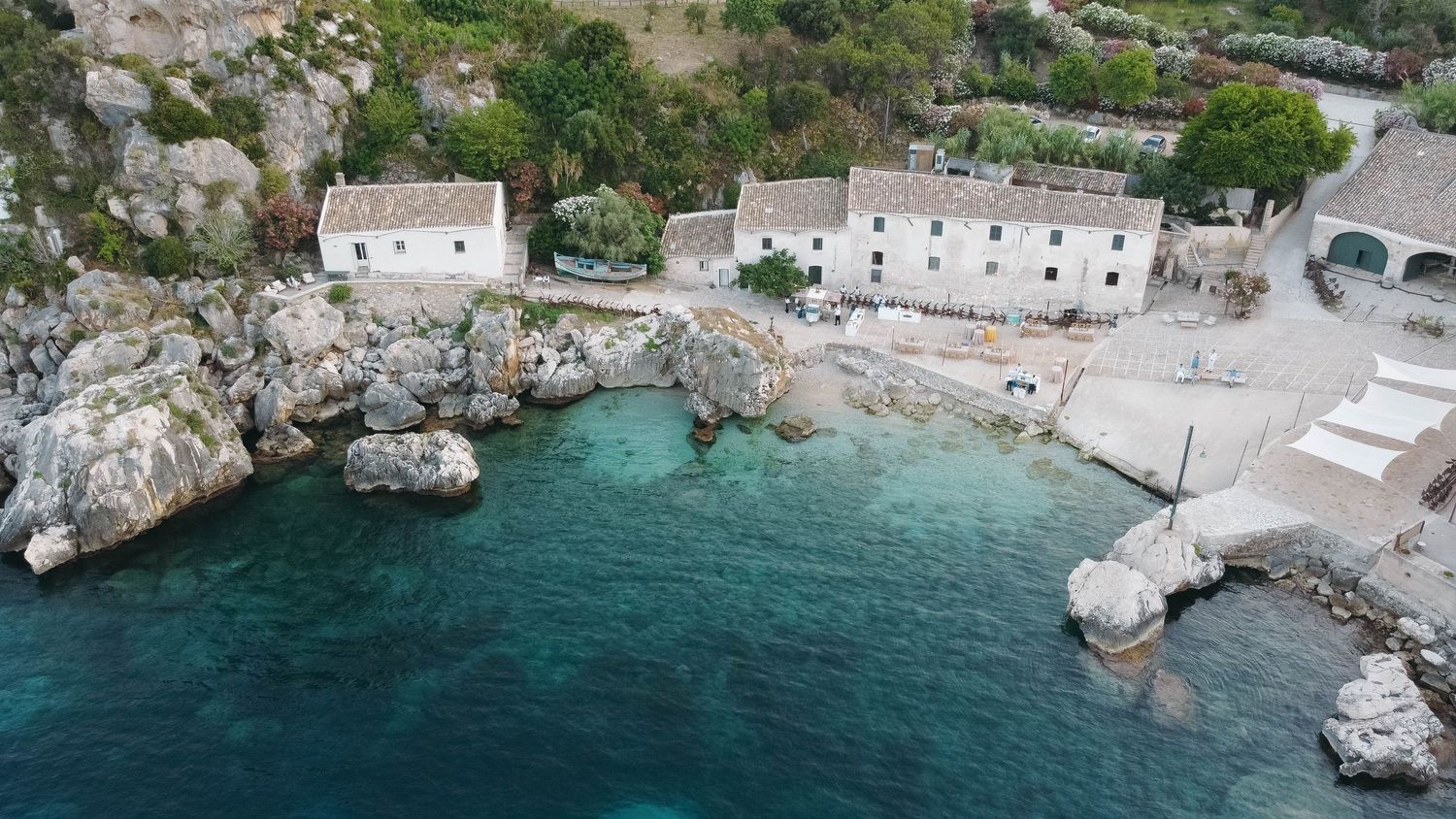 Panoramic coastal landscape showing white buildings integrated into rocky Mediterranean cliffside.
