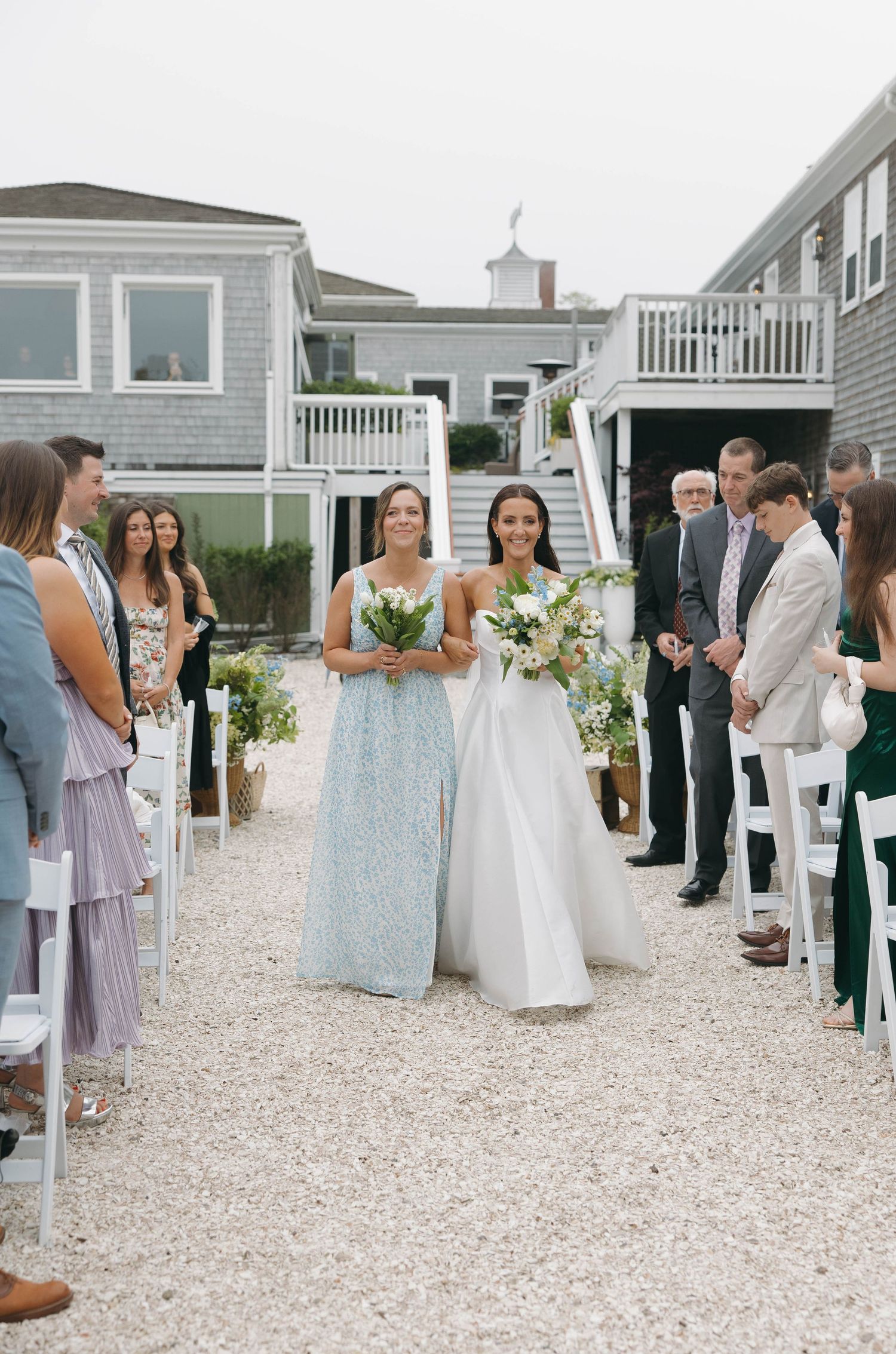 Wedding guests gathered on gravel courtyard between coastal beach houses.