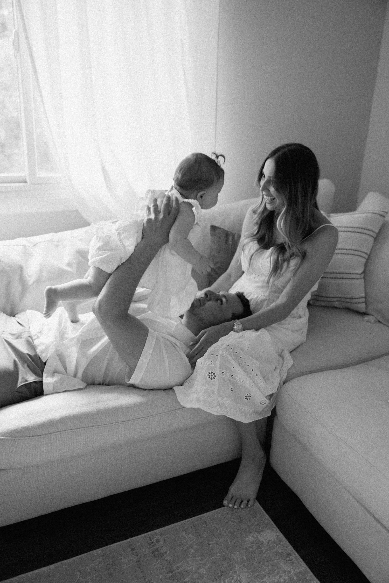 Black and white photo series of a relaxed moment on a white couch by a bright window.