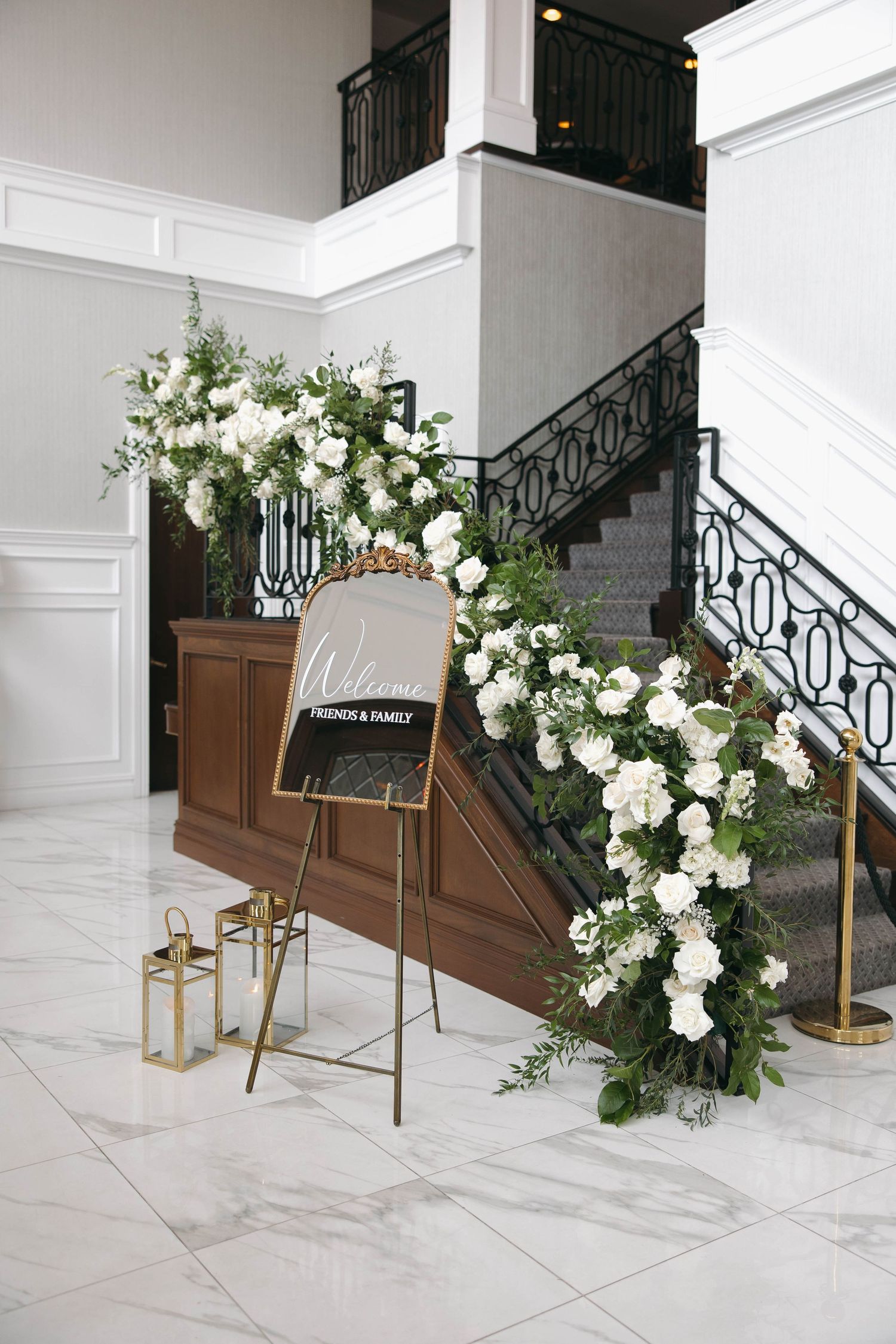Elegant staircase decorated with white floral arrangements and a welcome sign on an easel.