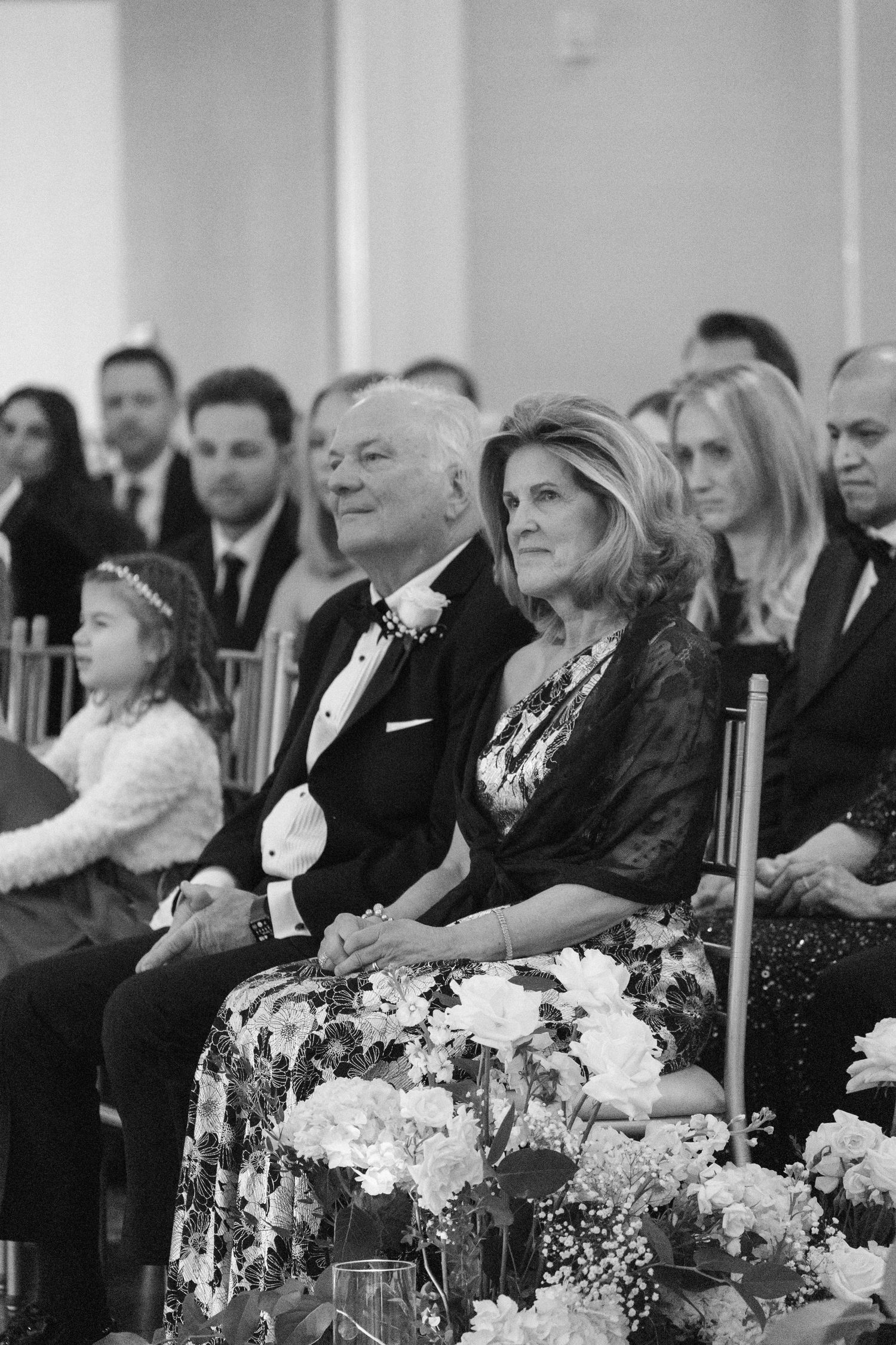 Wedding guests seated in formal attire with elegant white floral table decorations.