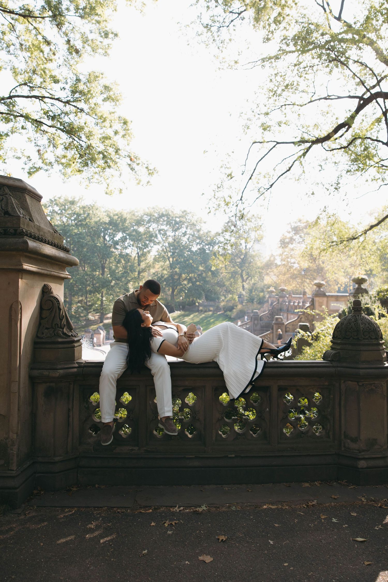 Couple posing on stone wall surrounded by trees in romantic photoshoot.
