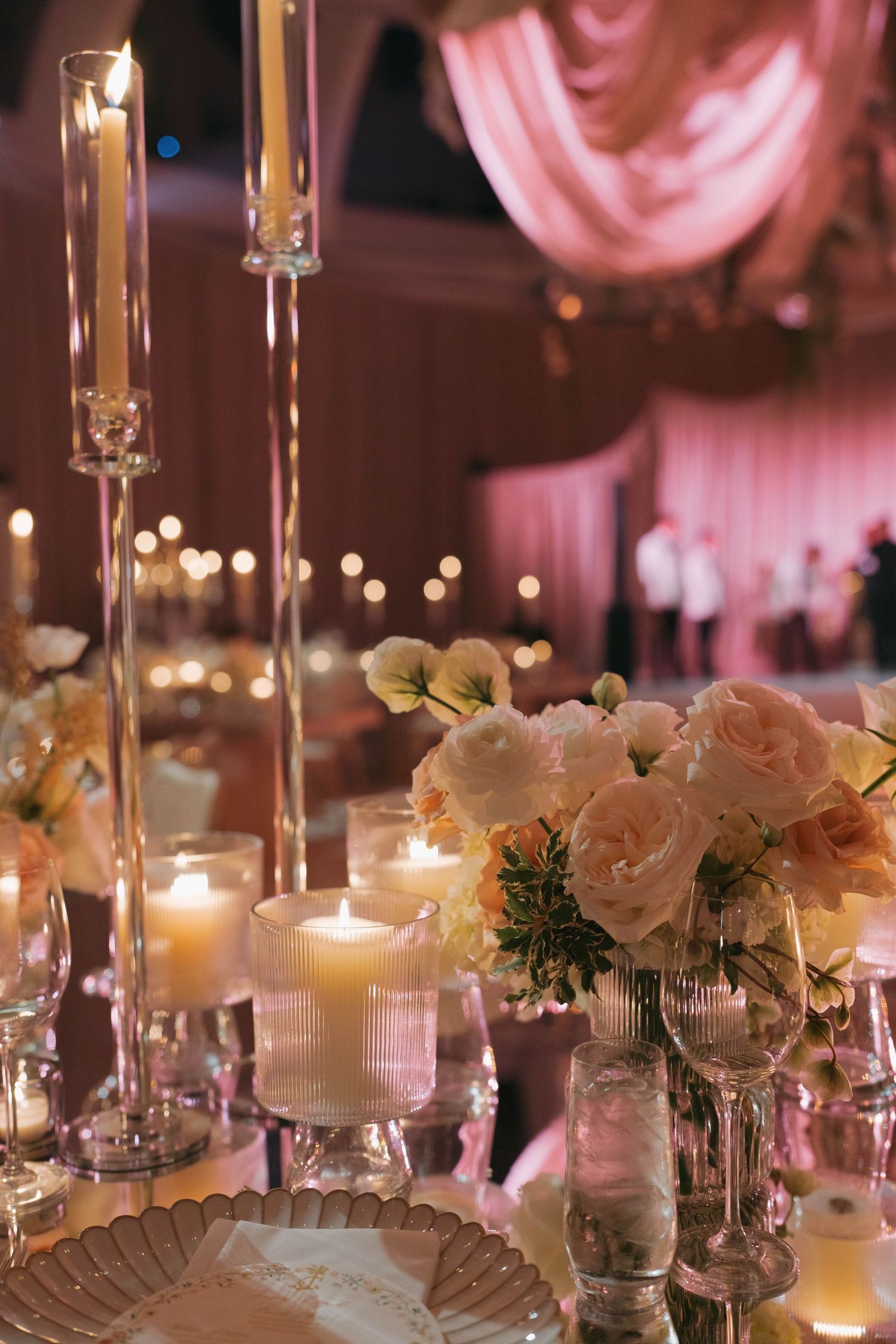 Close-up of romantic table decor featuring white roses, candles, and crystal candleholders.