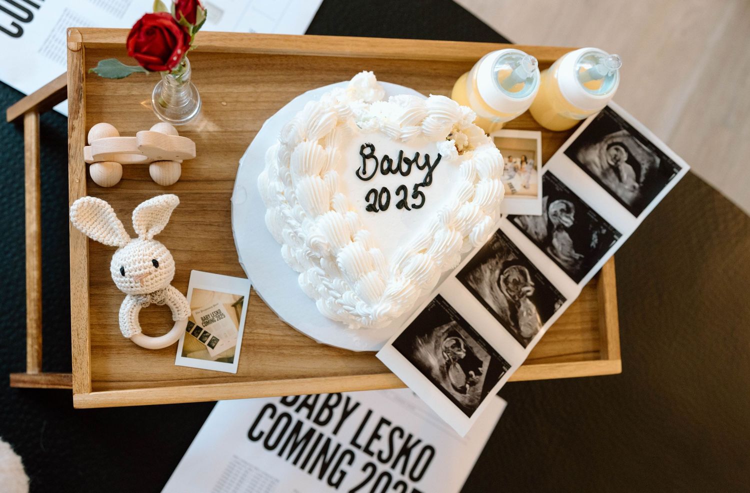 A wooden board displays pregnancy announcement items including ultrasound photos, a red rose, and a white bunny plush toy.