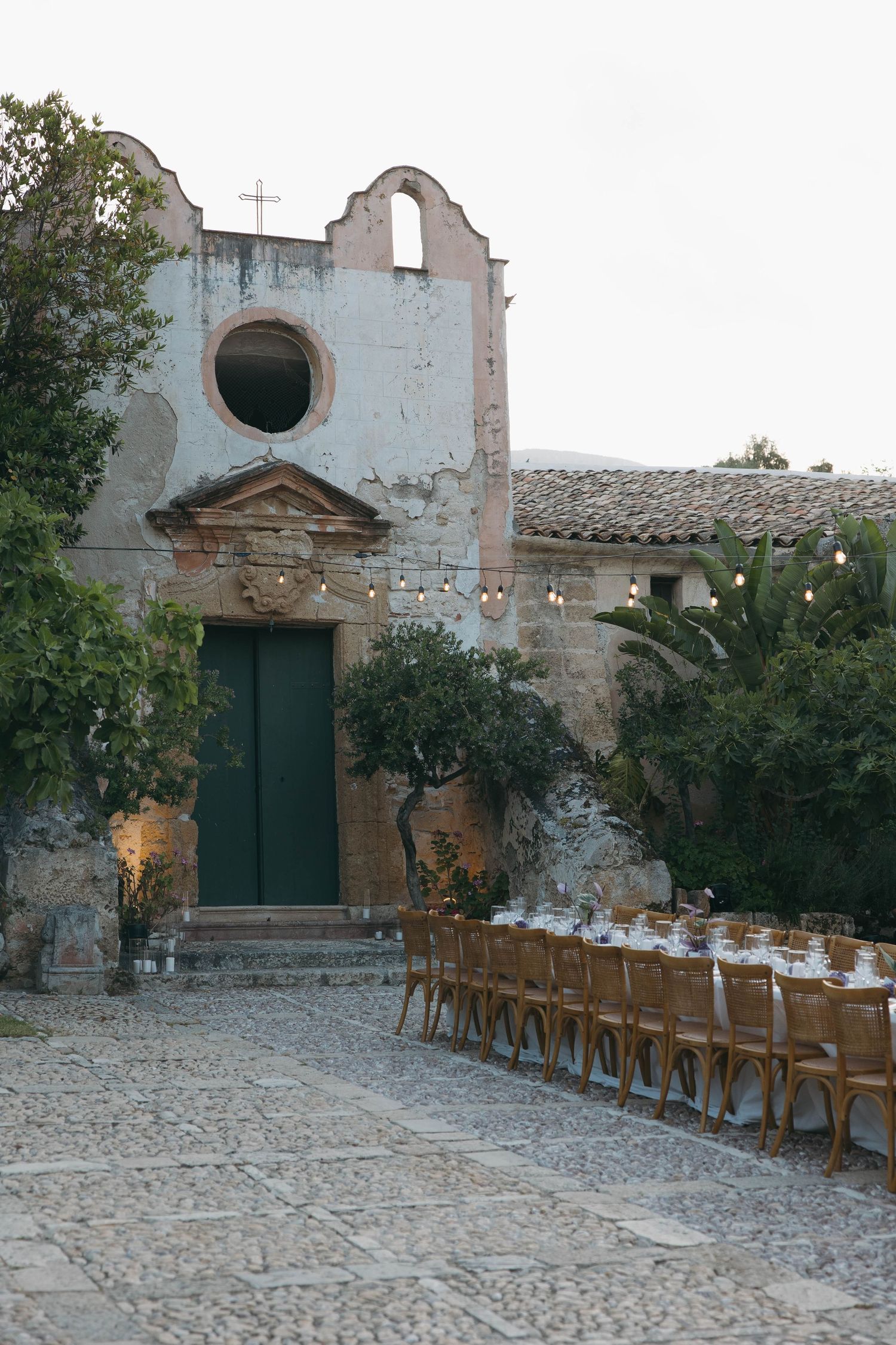 Rustic courtyard with wooden chairs arranged in front of an old stone church facade.