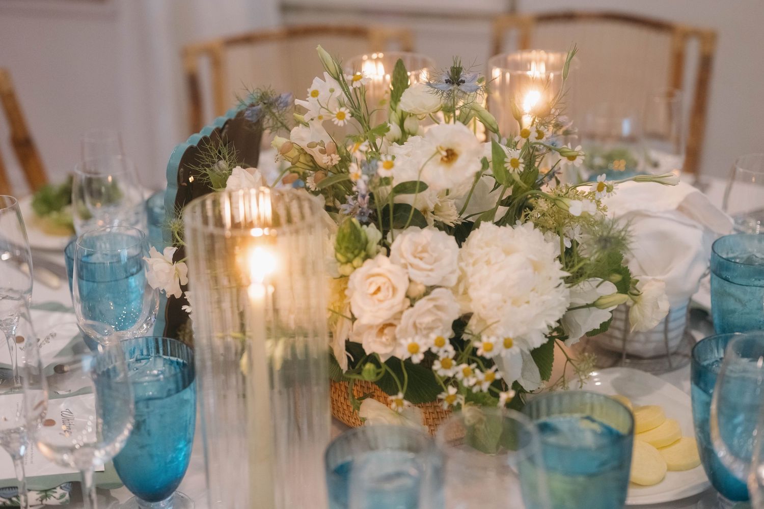 Wedding table decor featuring blue glassware and white floral arrangements with candlelight.