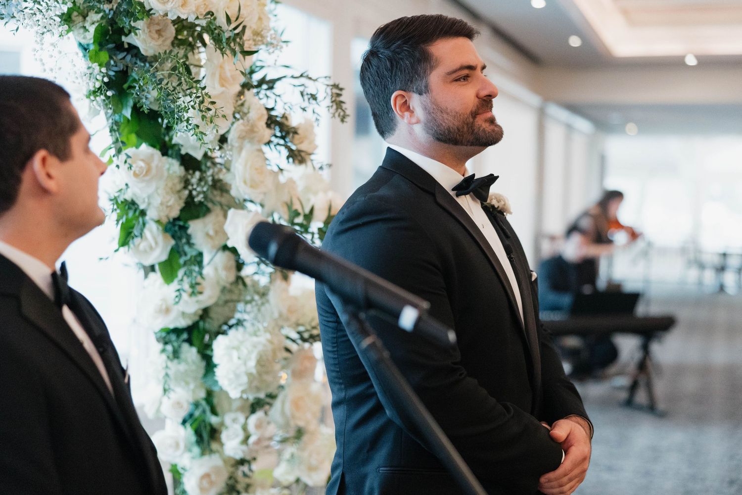 Elegant wedding ceremony in a bright ballroom with floral arch decorations and crystal chandeliers.