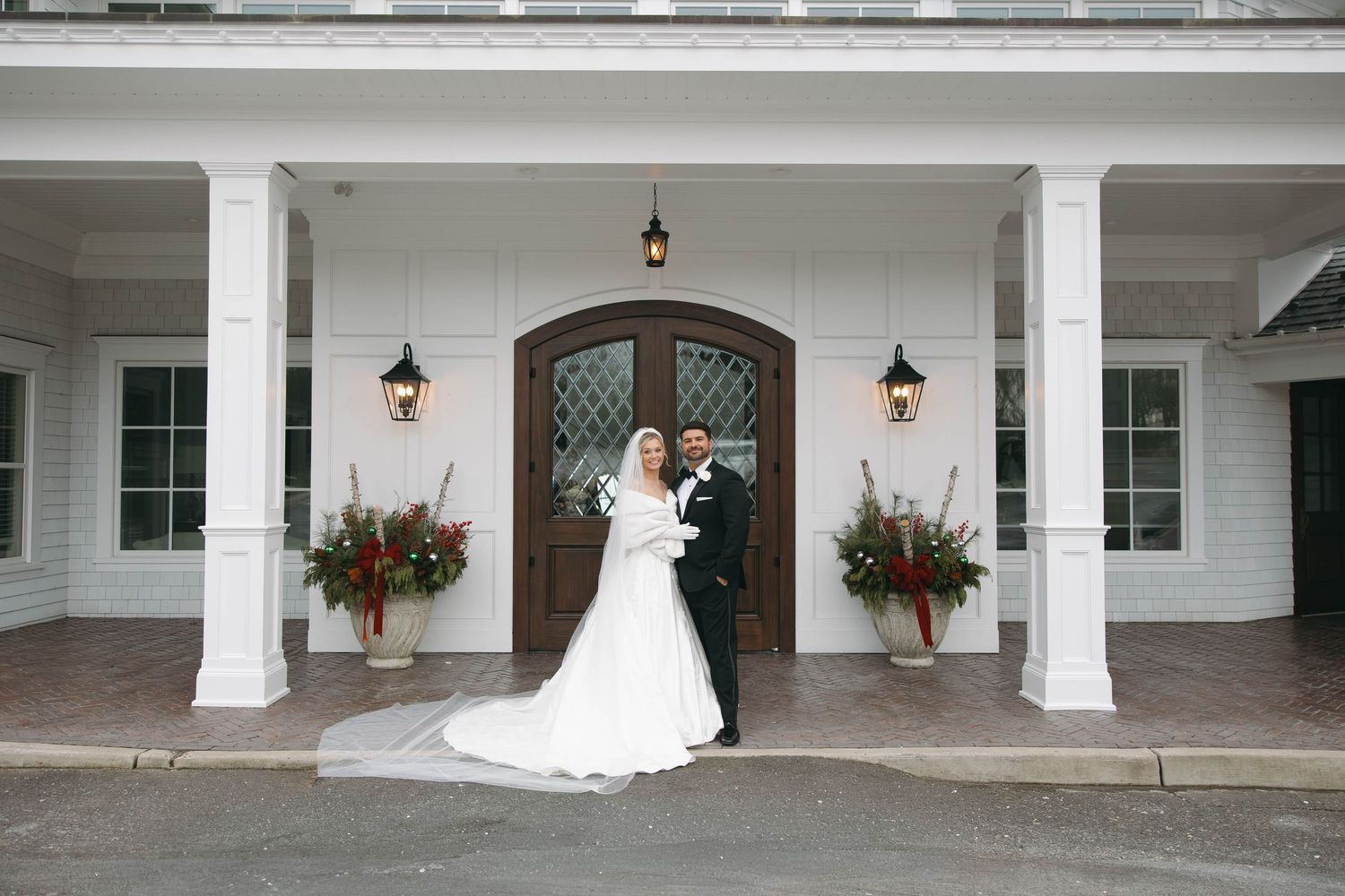 Wide shot of wedding venue exterior with white columns and hanging floral arrangements.