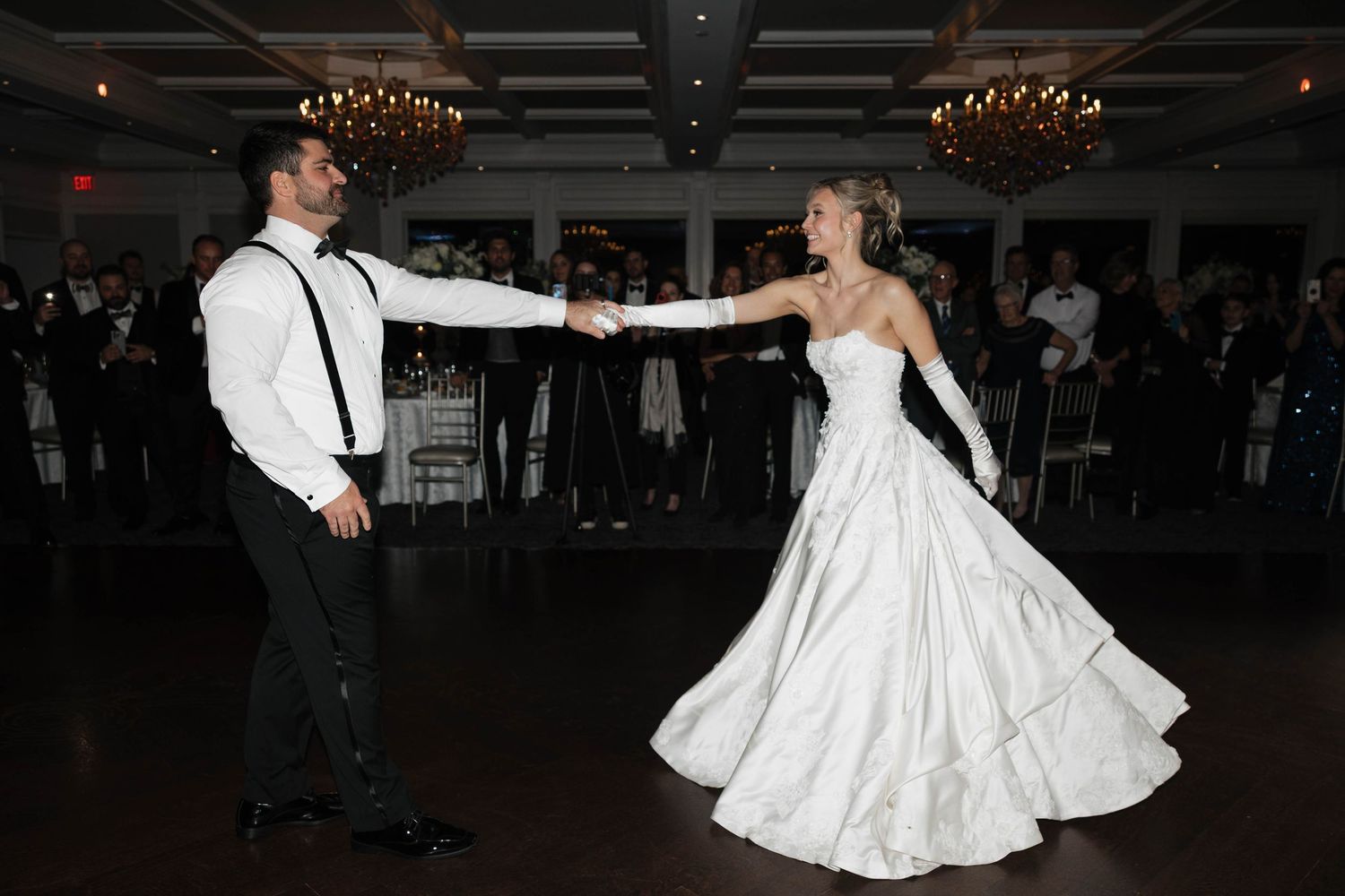 Newlyweds dance together in a ballroom with elegant lighting and decor.