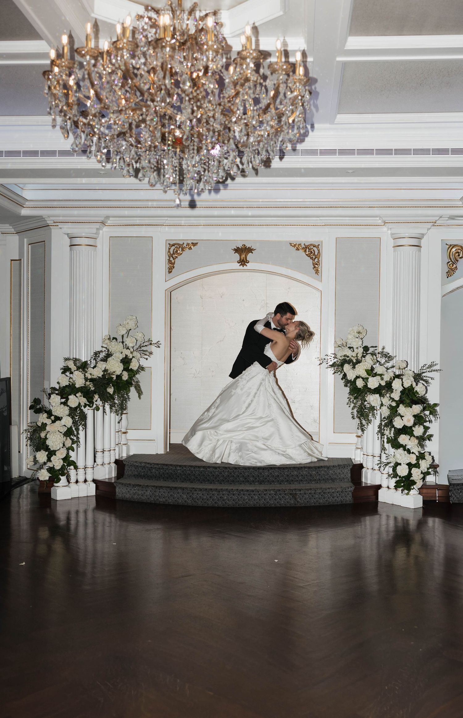 Elegant ballroom wedding scene with crystal chandelier and floral arch decorations.