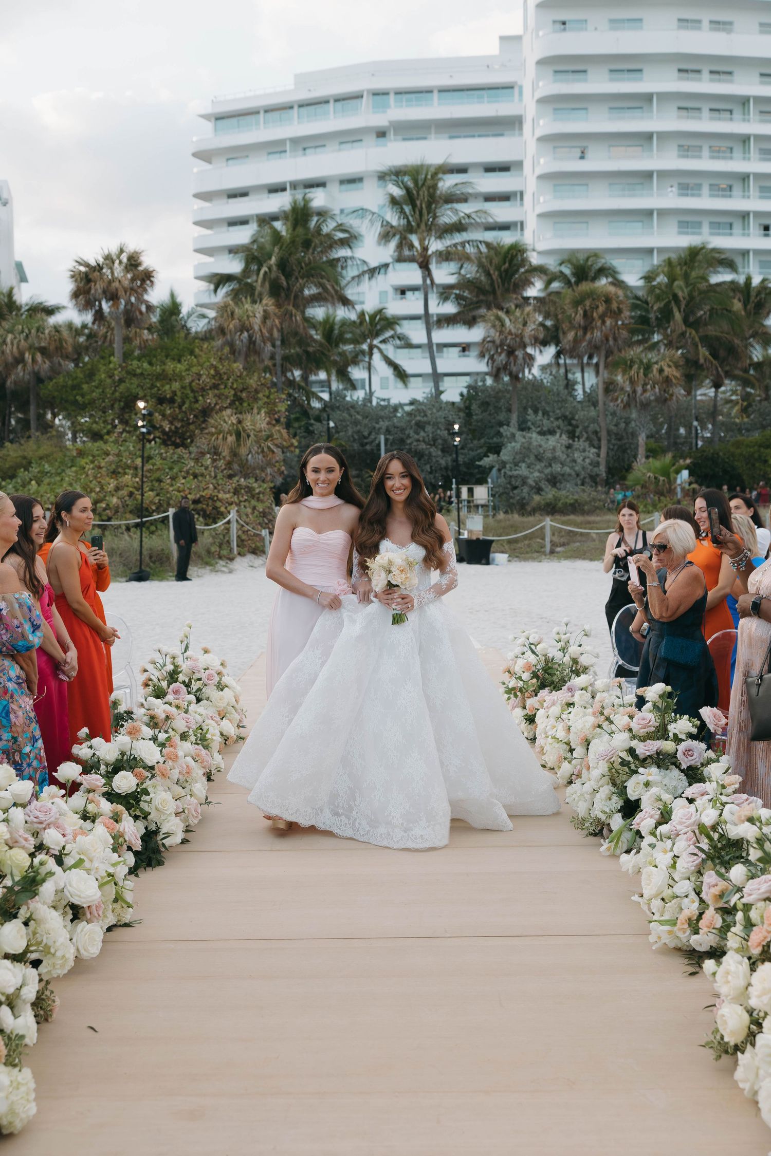 Wedding ceremony setup with white floral arrangements and palm trees against modern buildings.