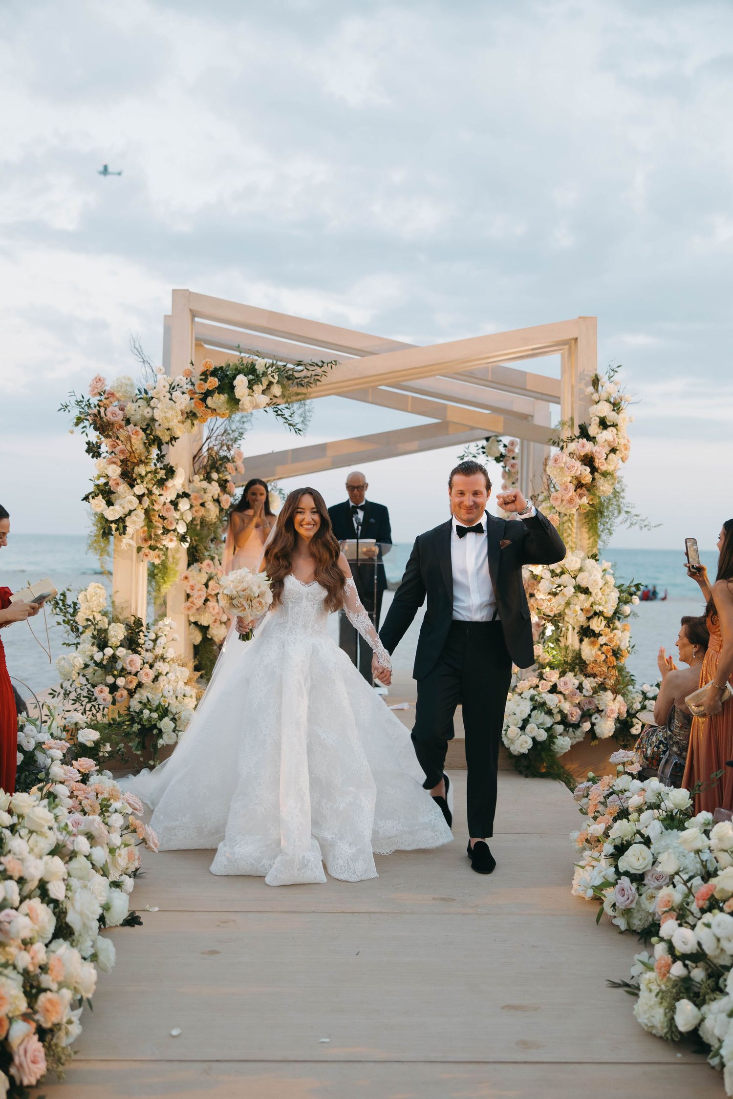 Wedding celebration moment captured under a beachside pergola with elegant floral decorations.