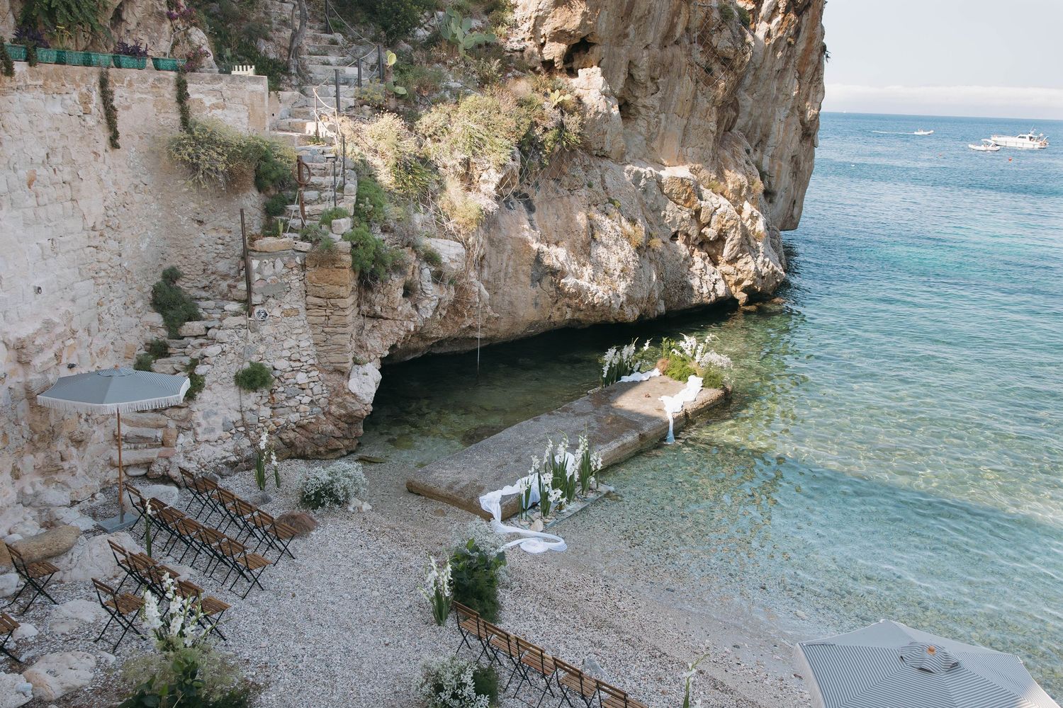 Scenic coastal view through stone ruins showing turquoise waters and boats in the distance.