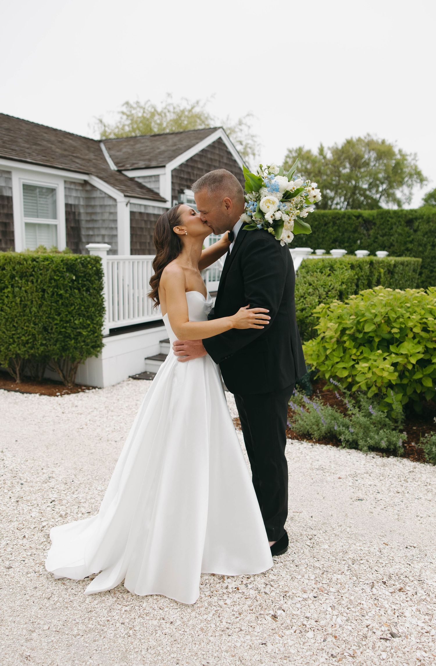 Wedding couple shares intimate moments on white gravel path by manicured hedges.