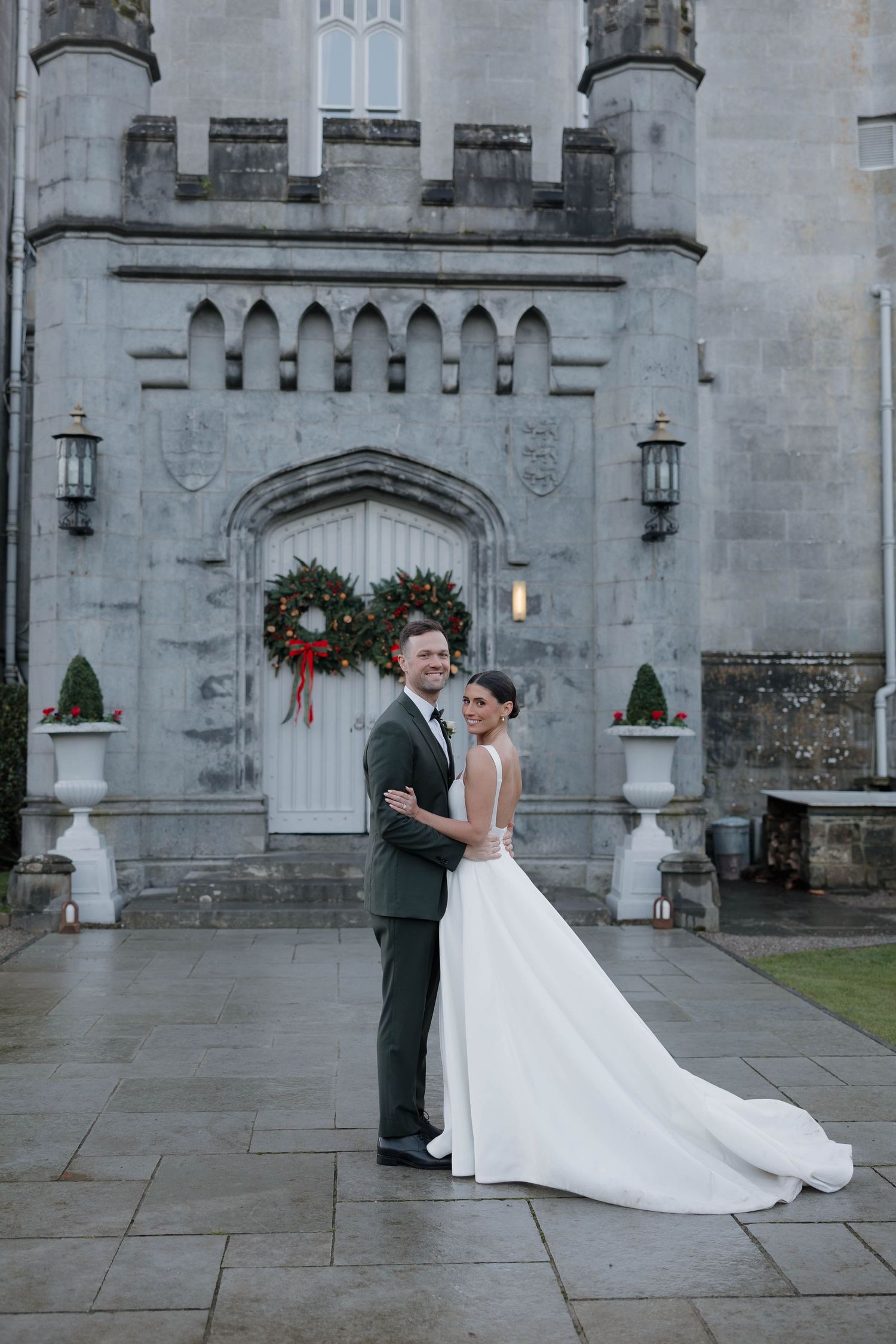 Wedding couple poses in front of gothic castle entrance with holiday decorations.