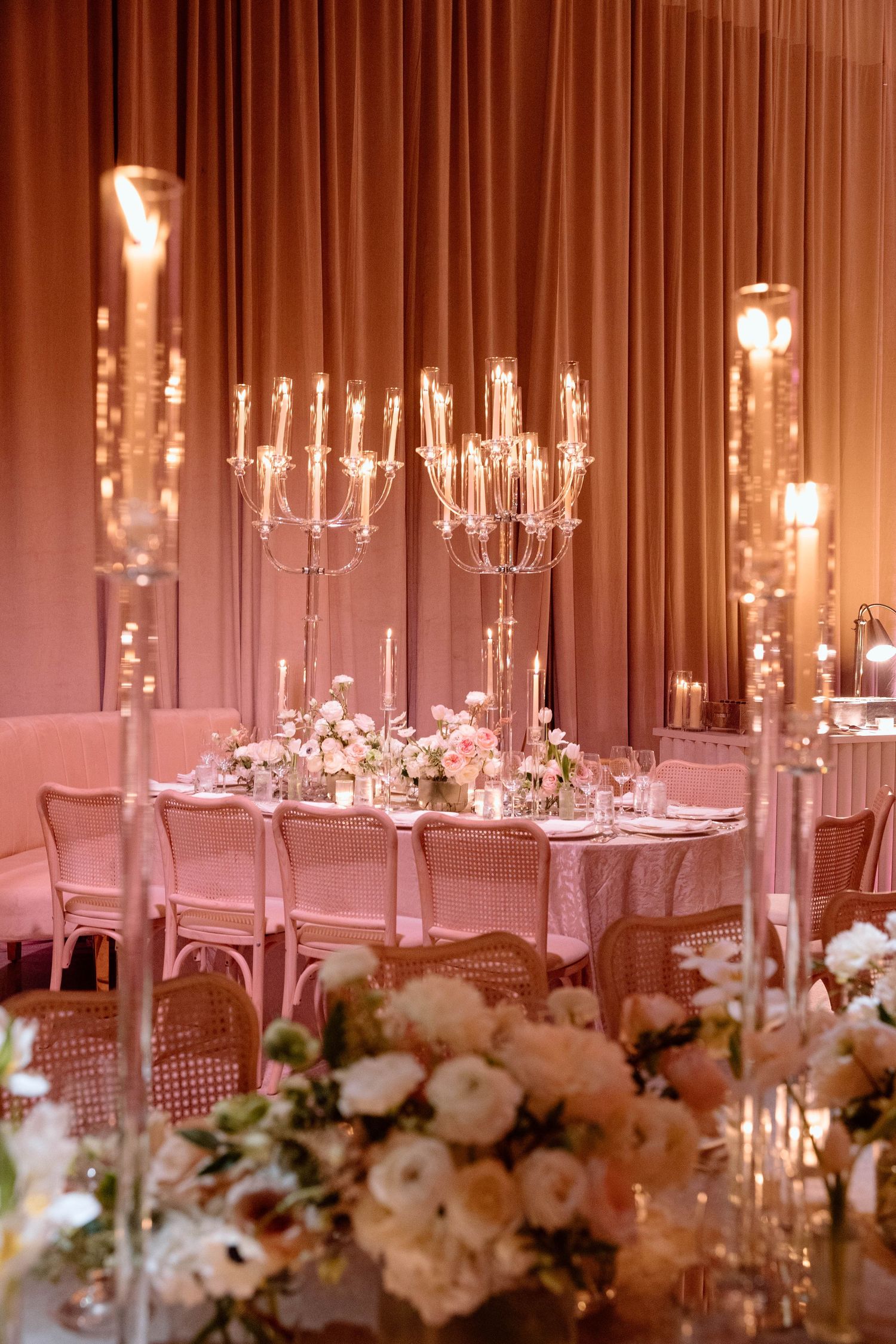 Crystal candelabras and white floral centerpieces line elegant reception tables in warm ambient lighting.