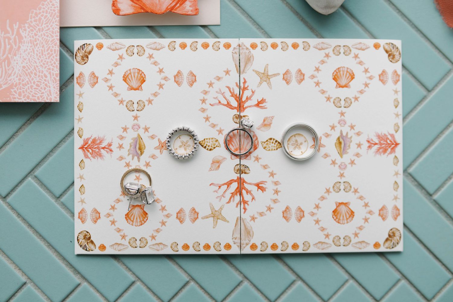 Wedding rings displayed on seashell patterned card with coral accents.