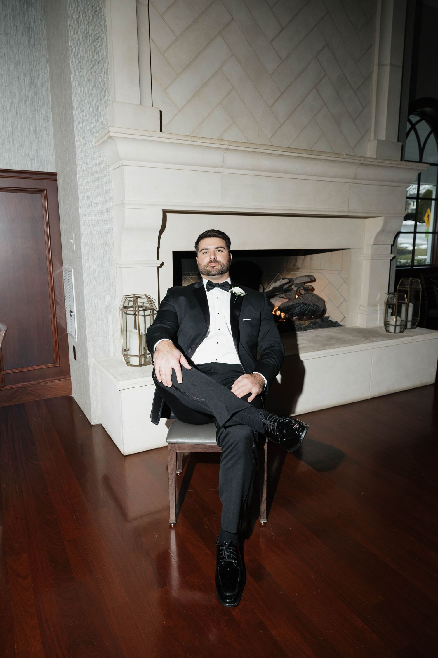 Wide-angle shots of a groom sitting against a white wall in formal attire.