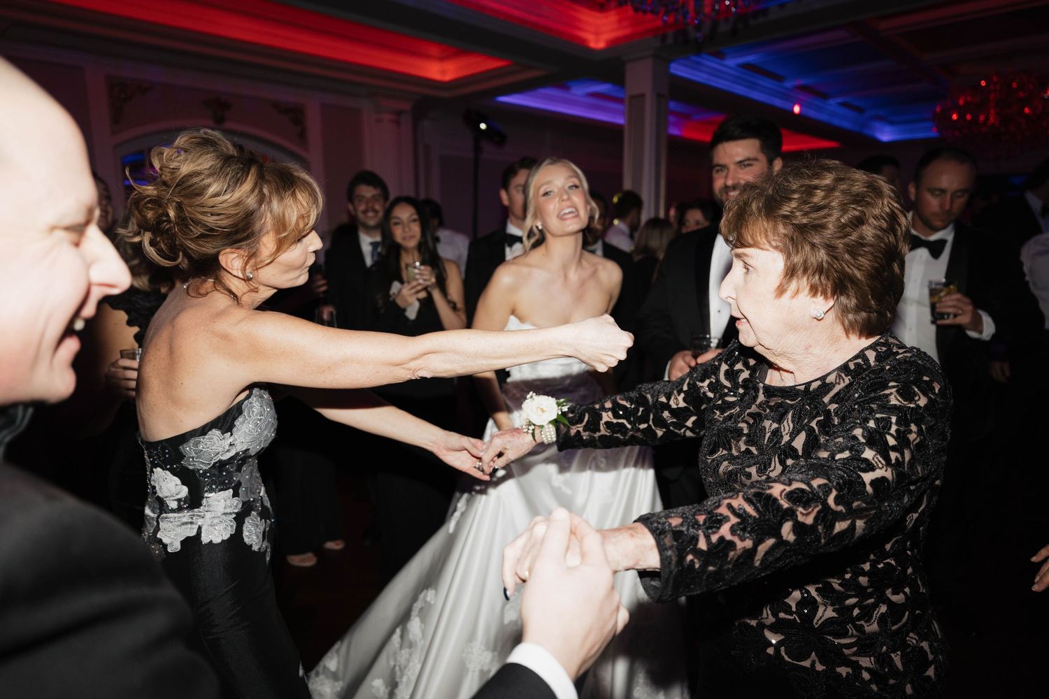 Wedding celebration with guests dancing under colorful lighting in elegant ballroom.