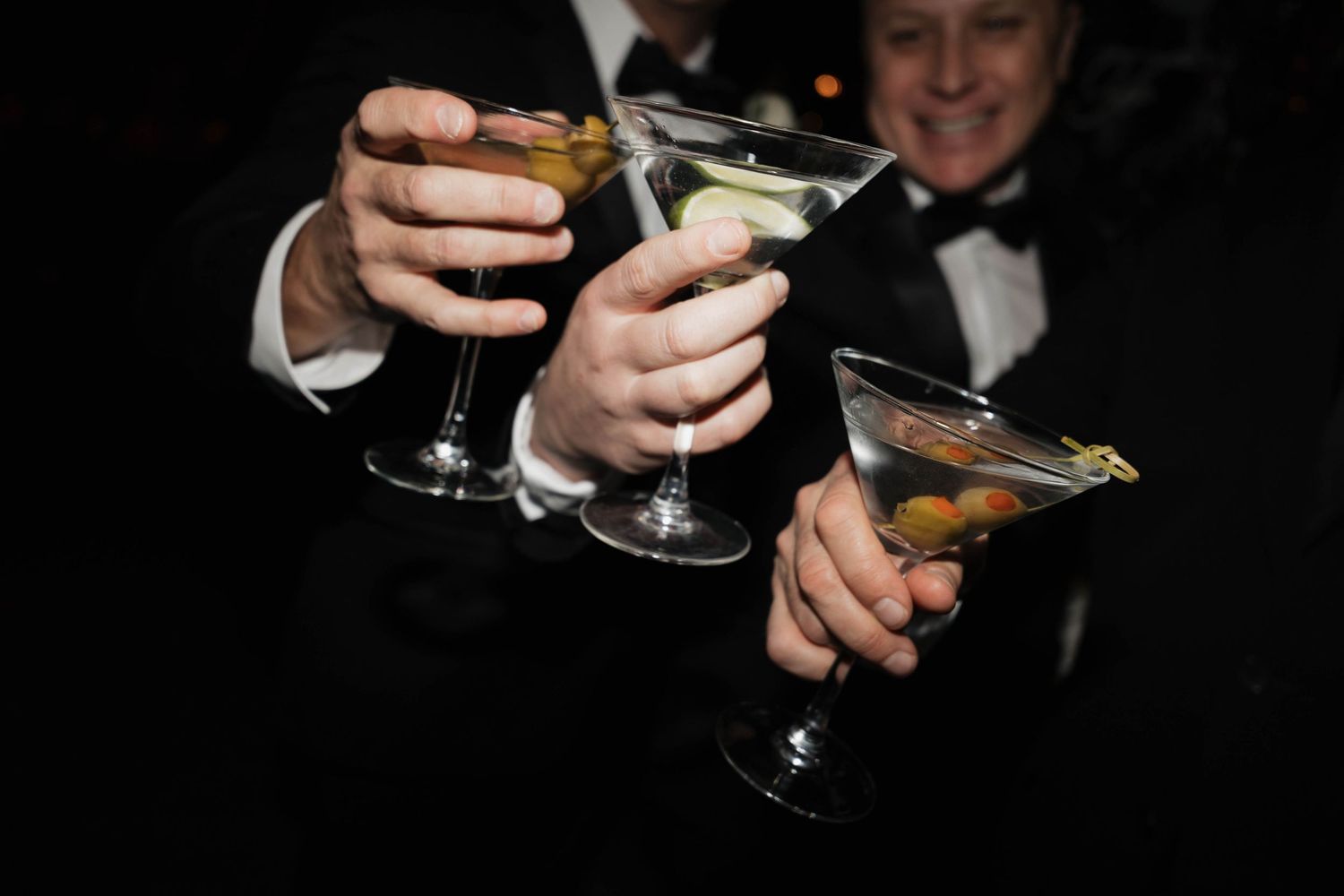 Three cocktail glasses being toasted at formal event.