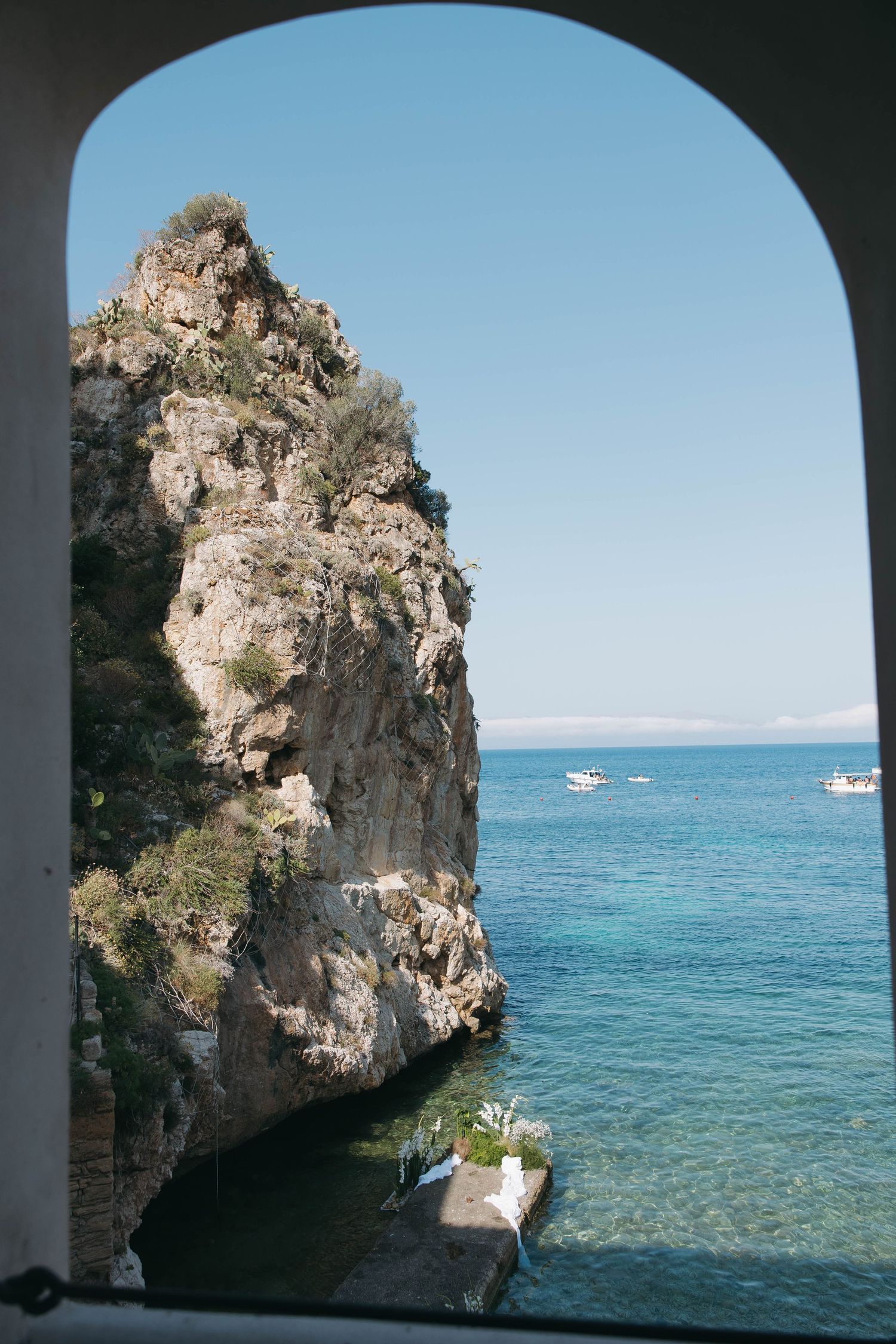 Arched stone doorway frames a stunning view of blue Mediterranean waters and rocky coastline.
