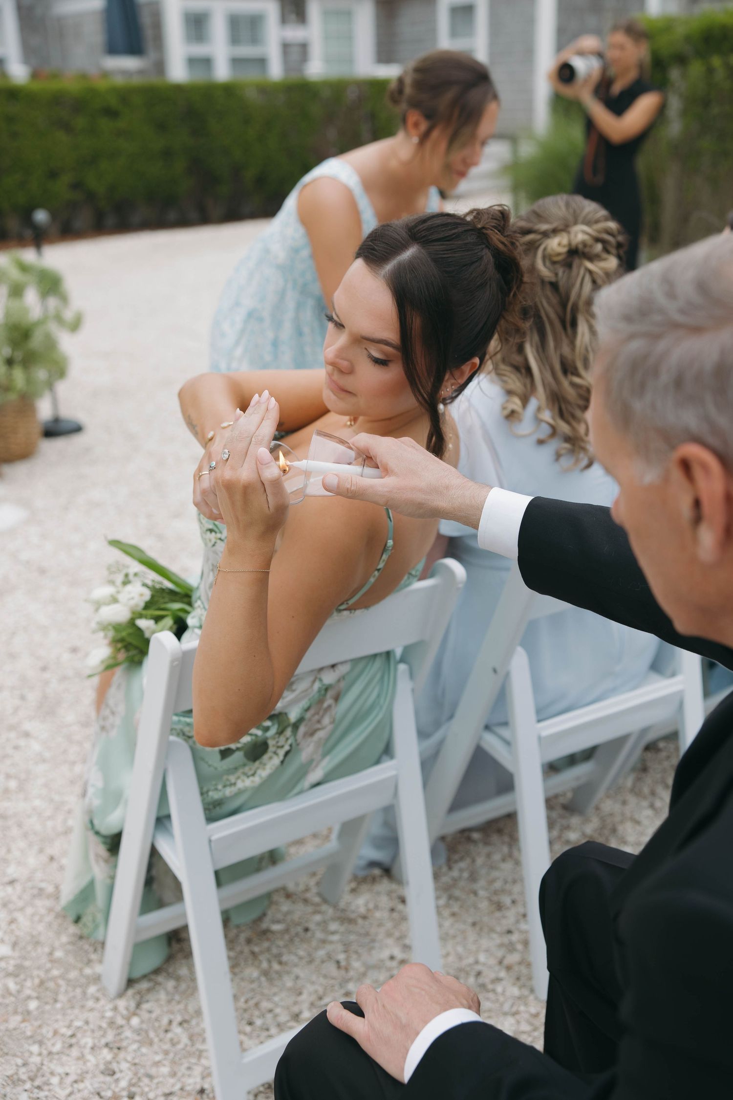 Wedding guests seated in white folding chairs during outdoor ceremony.