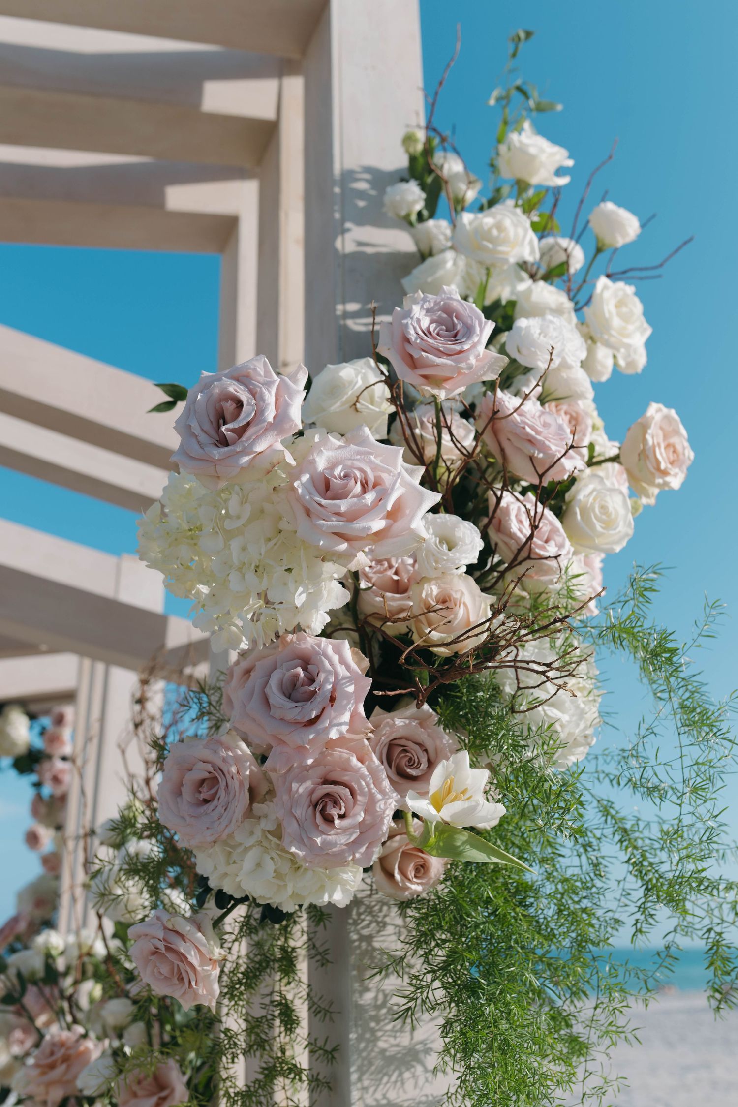 Romantic blush and white roses adorning a wedding arch against bright blue sky.