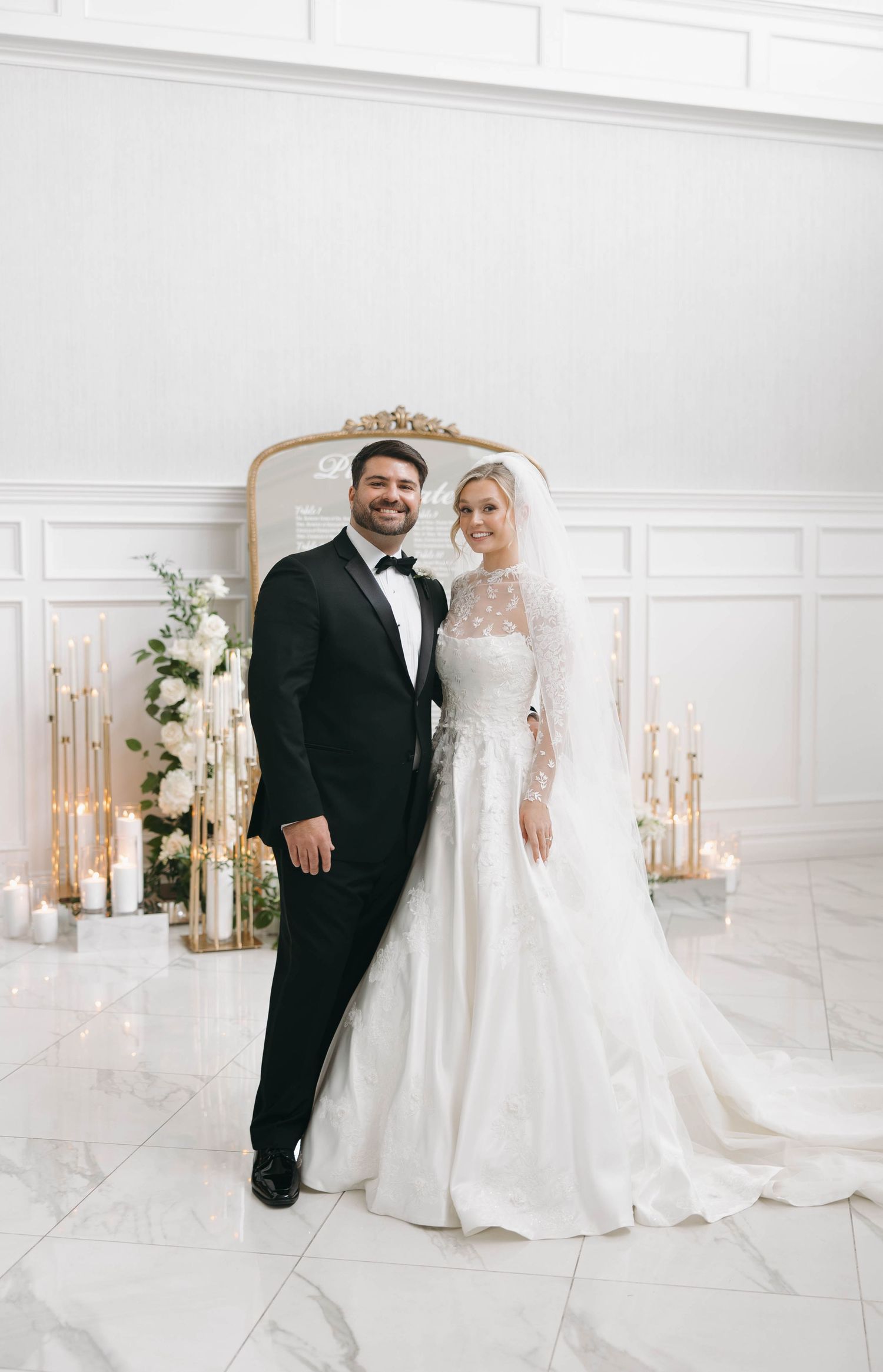 Wedding couple poses in an elegant white room with ornate decor and marble floors.