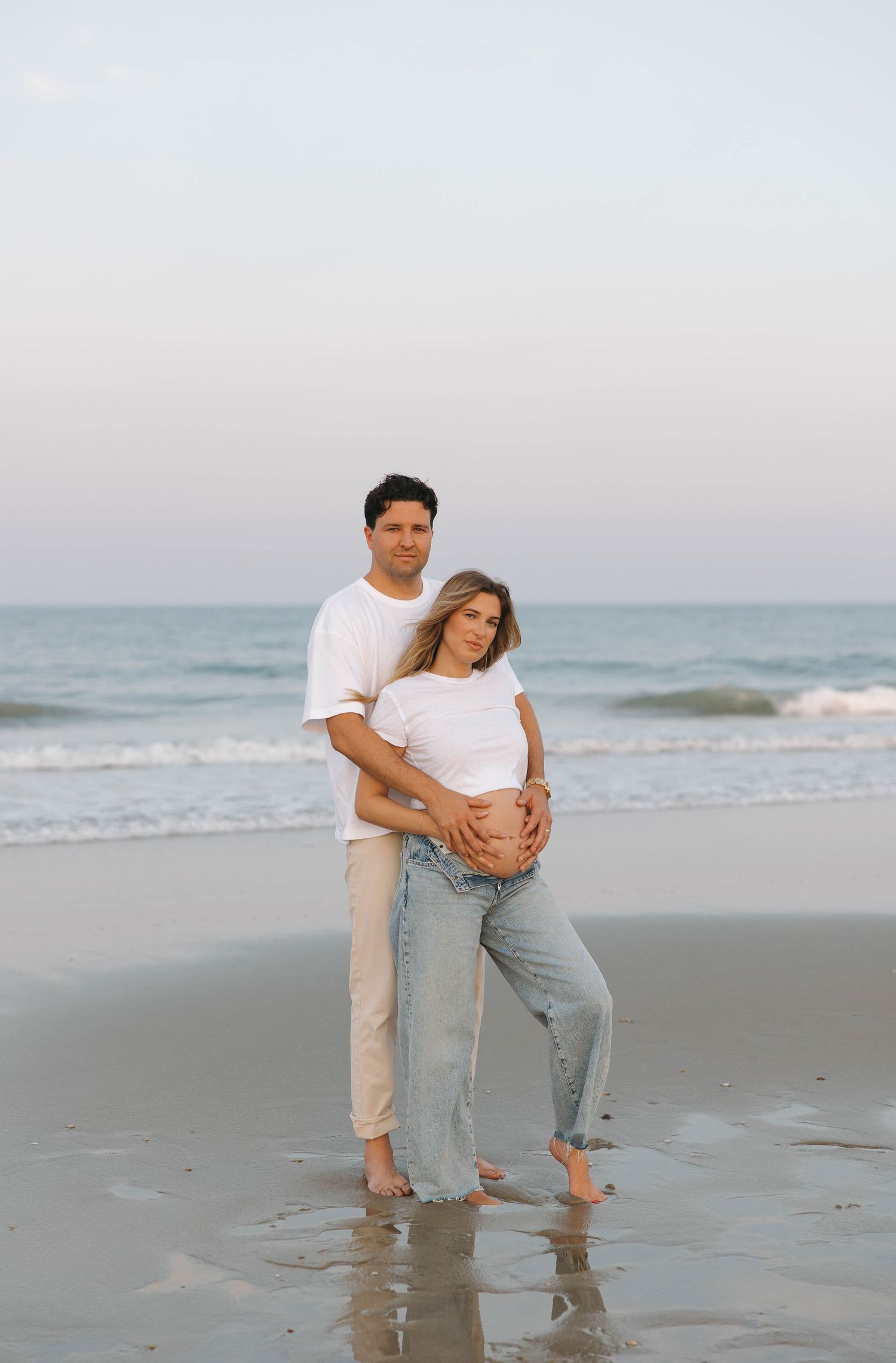Playful couple posing together on a serene beach during a casual photoshoot.