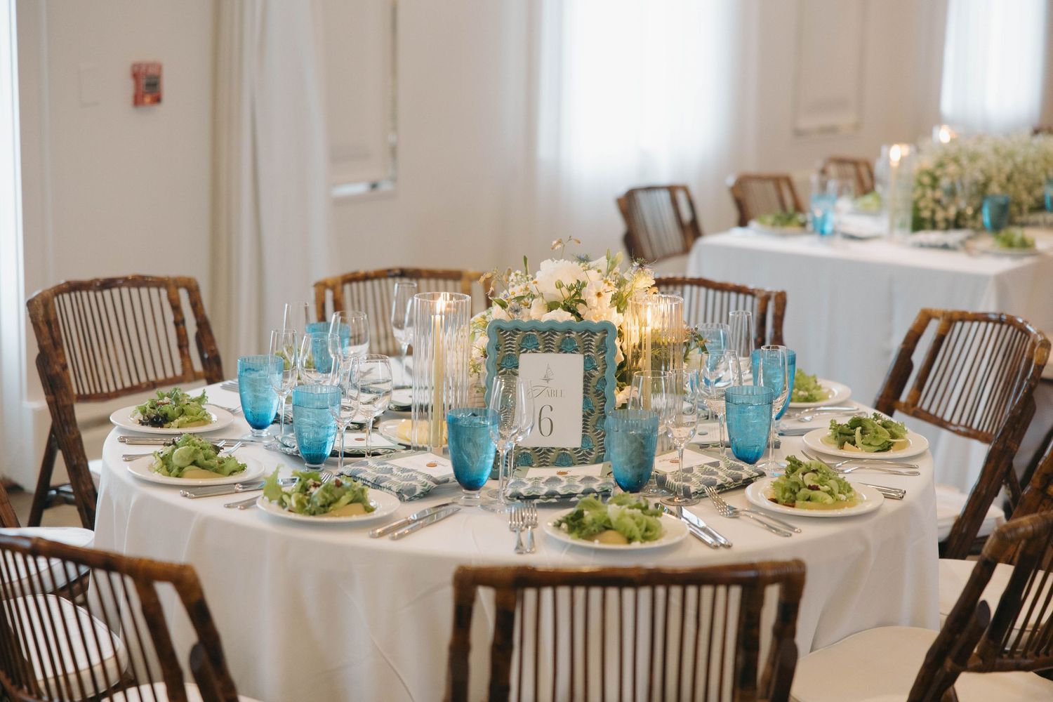 Elegant wedding reception tables set with white linens and wooden chairs in bright dining room.
