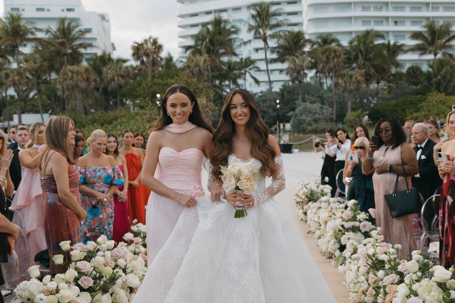 Wedding ceremony on beach with tropical landscaping and modern architecture in background.