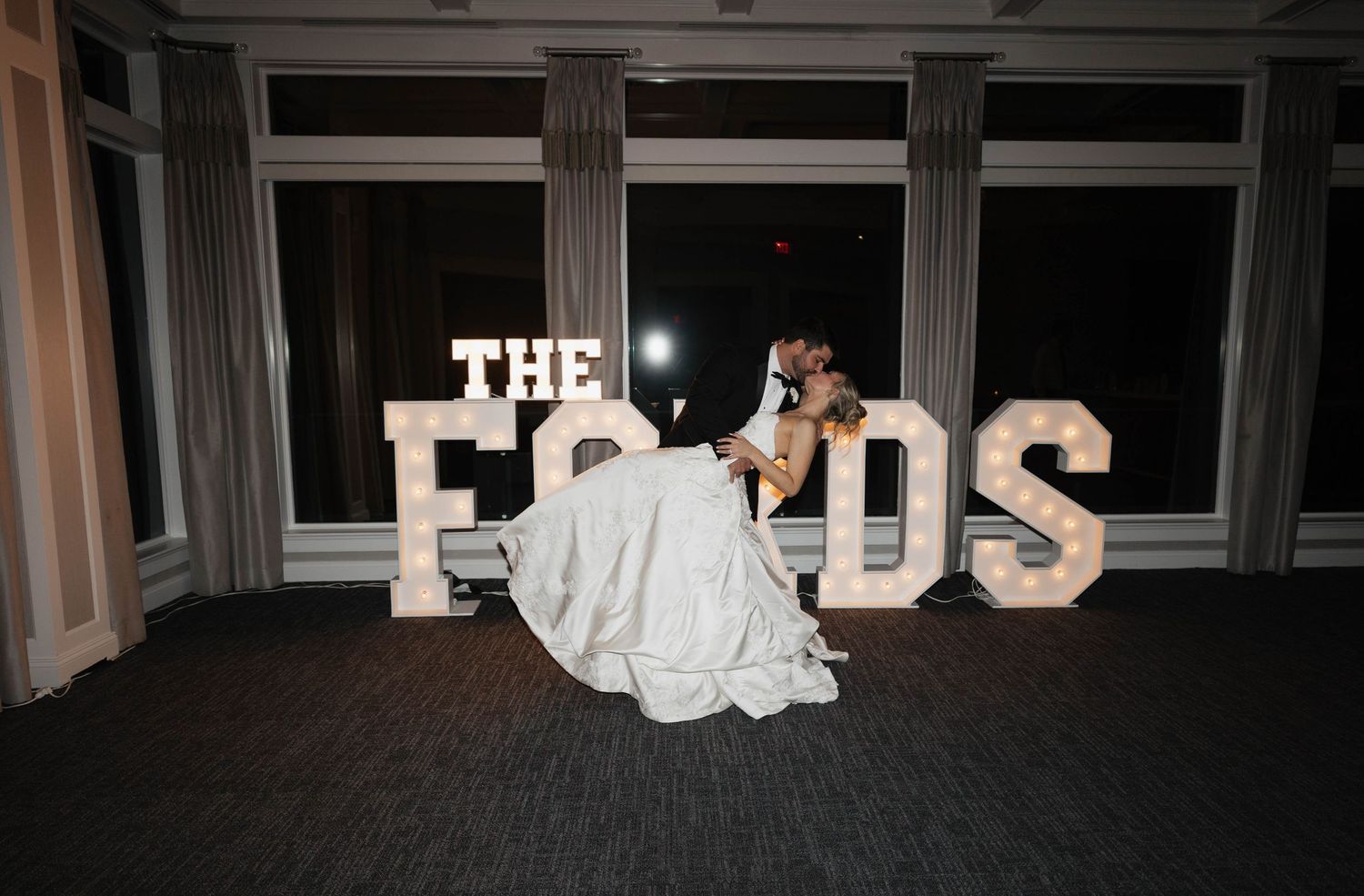 Wedding couple dances in front of illuminated letters spelling 'THE FORDS' at their reception.