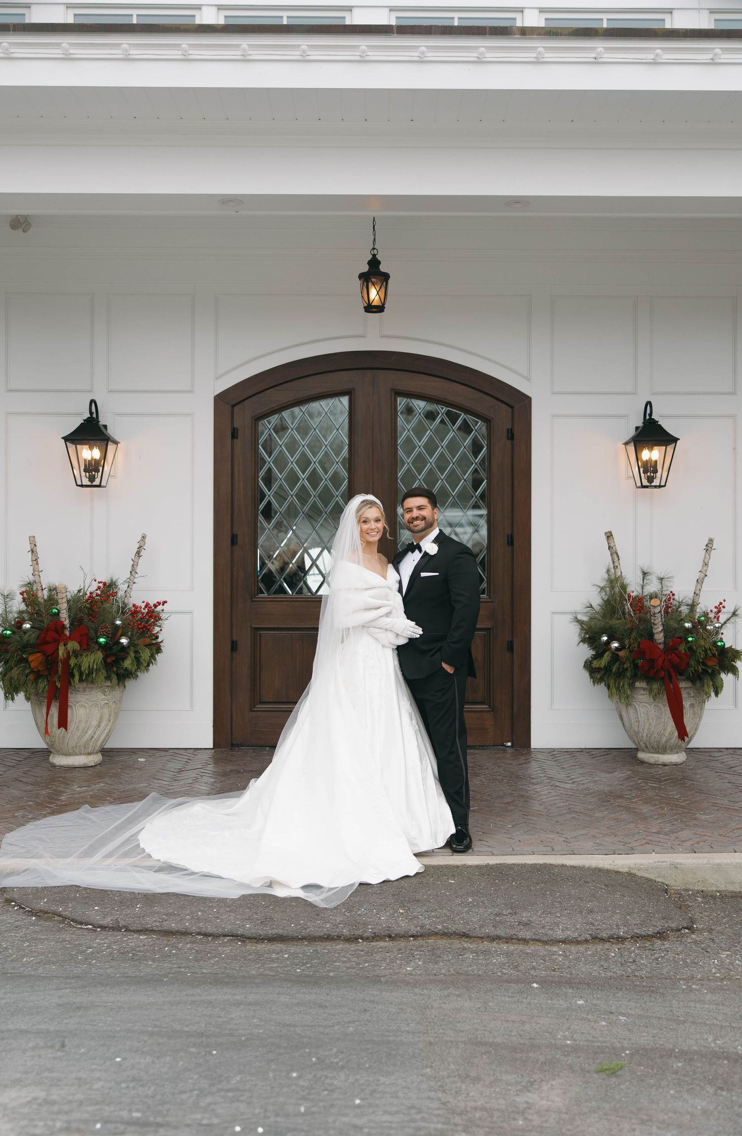 Wedding couple poses beneath arched doorway decorated with holiday floral arrangements.