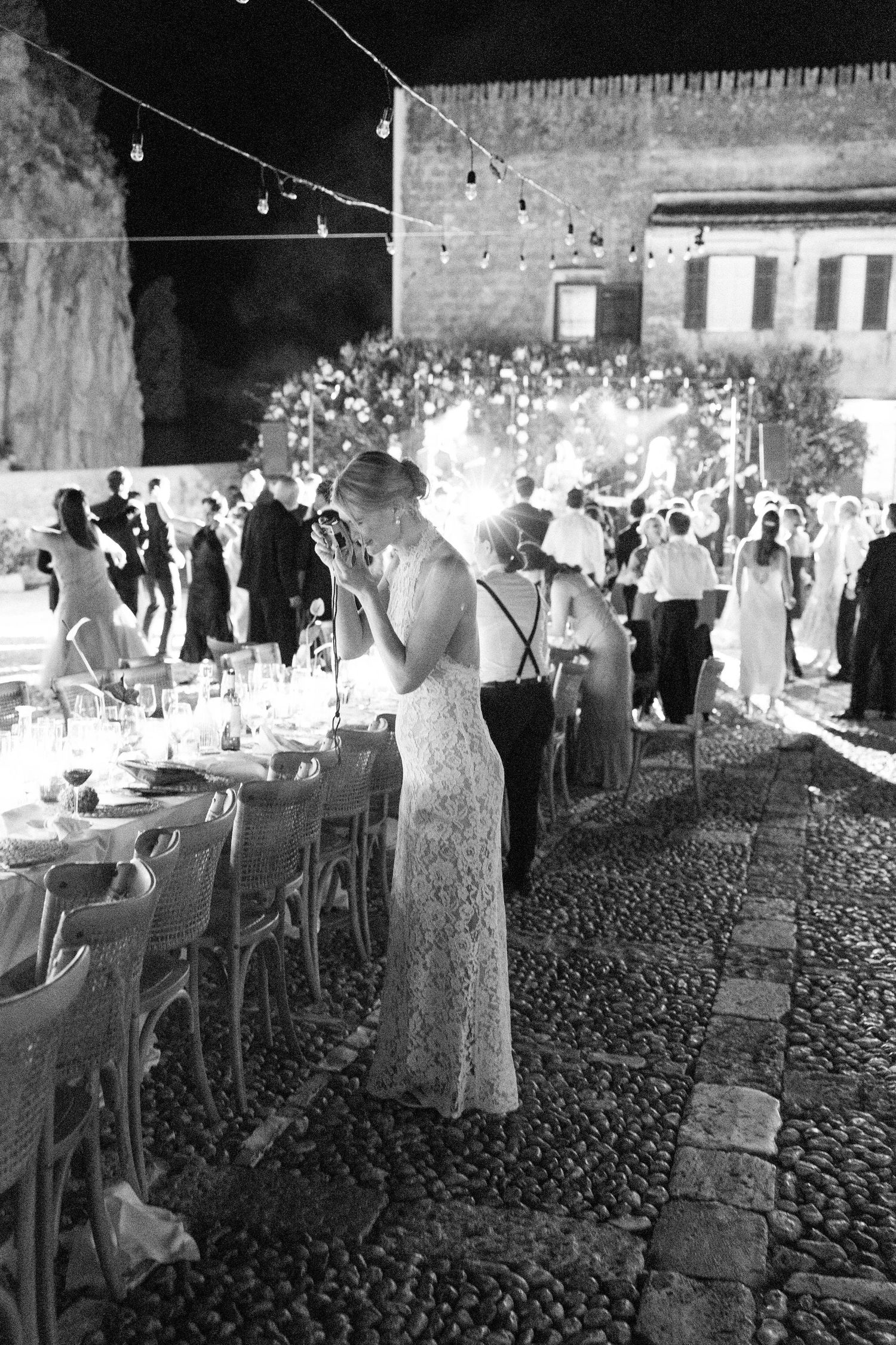 Elegant outdoor reception with tables set against stone walls and string lights overhead.
