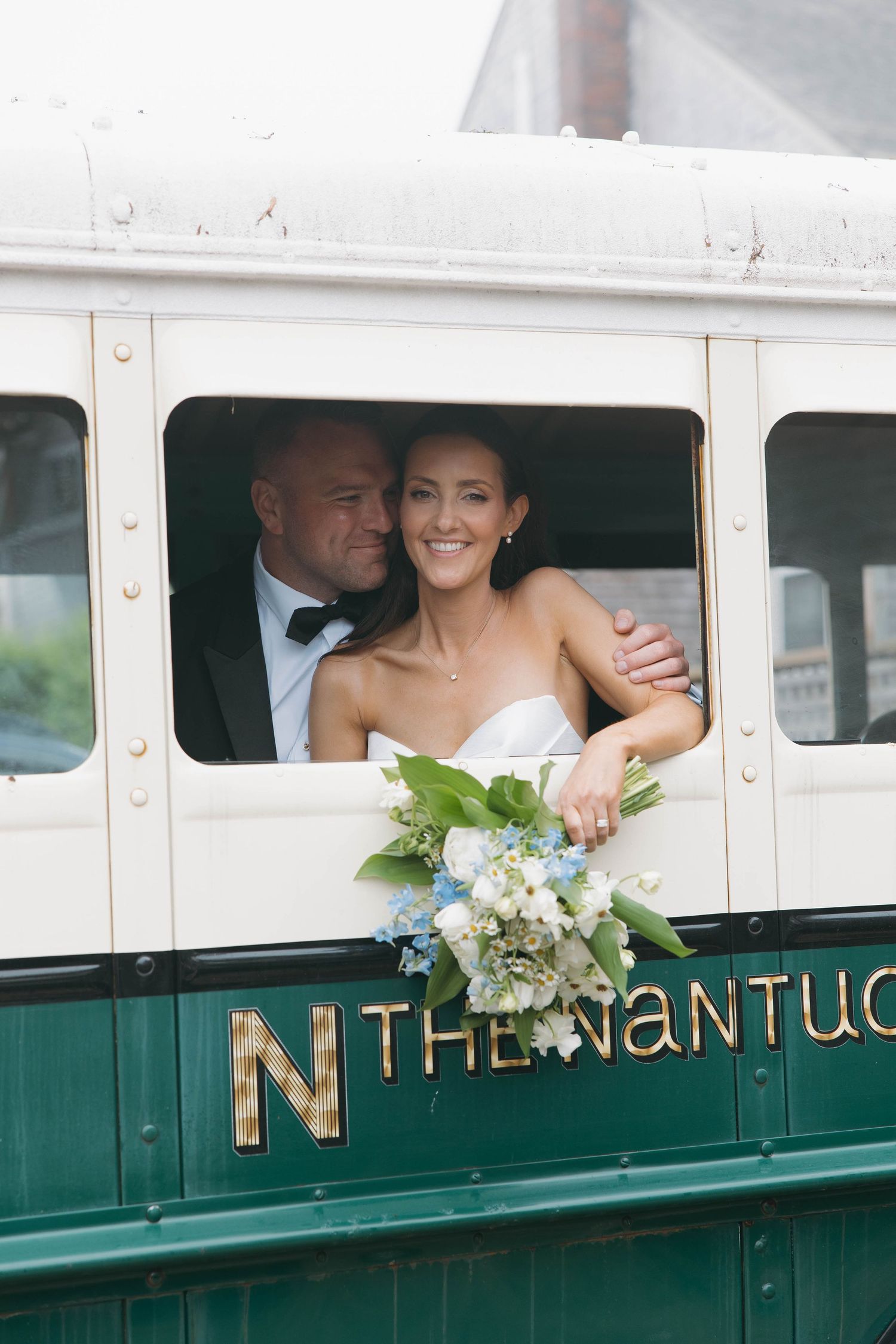 Wedding couple peeks out windows of vintage green and white trolley labeled Nantucket.