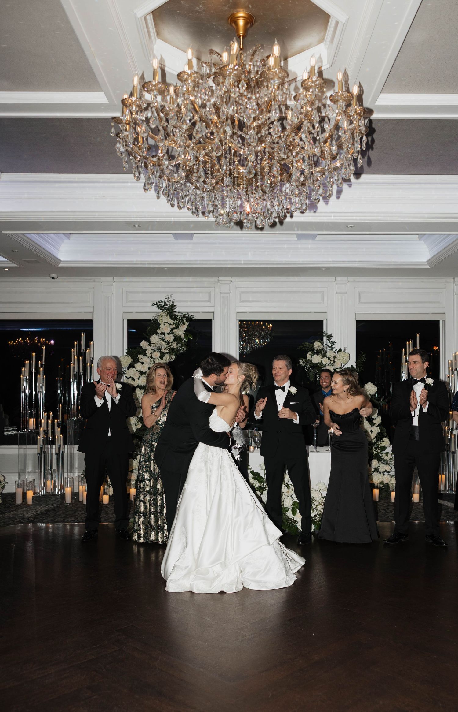 Wedding reception dance floor scene with crystal chandeliers and elegant white decor.